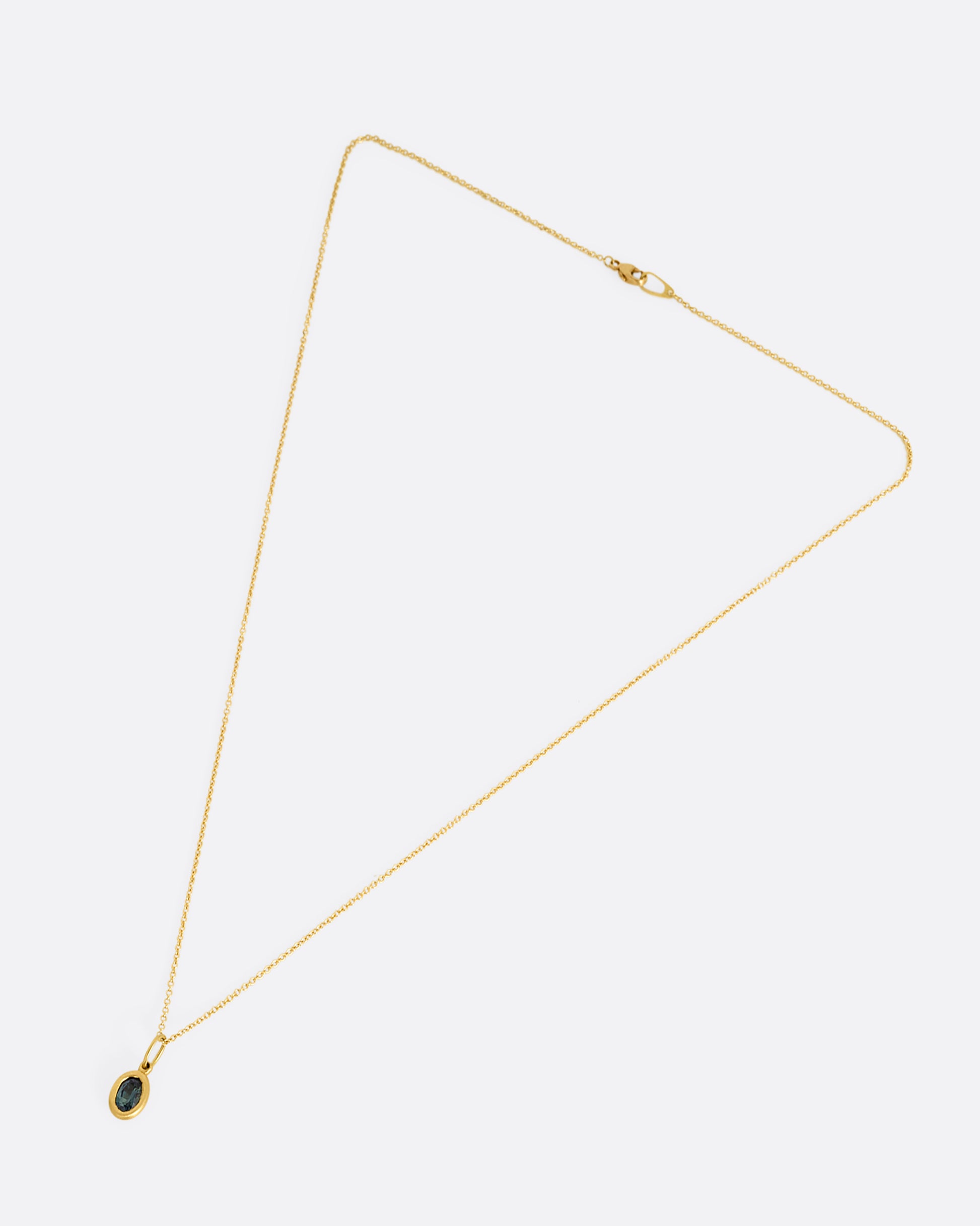 A yellow gold cable chain necklace with a bezel set oval blue green sapphire. Shown lying flat clasped from the front.