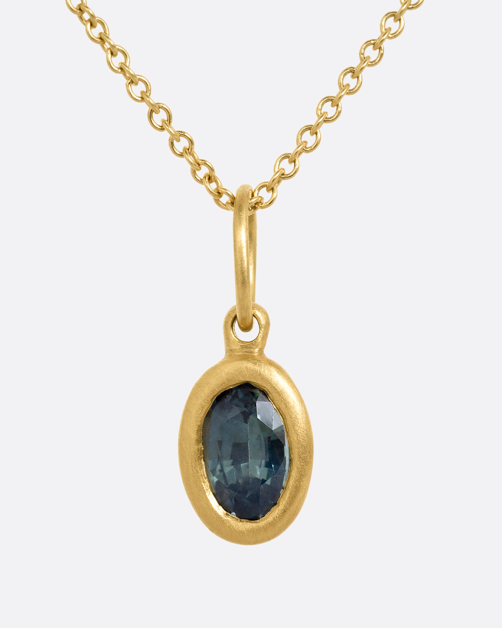 A yellow gold cable chain necklace with a bezel set oval blue green sapphire. Shown from the front.