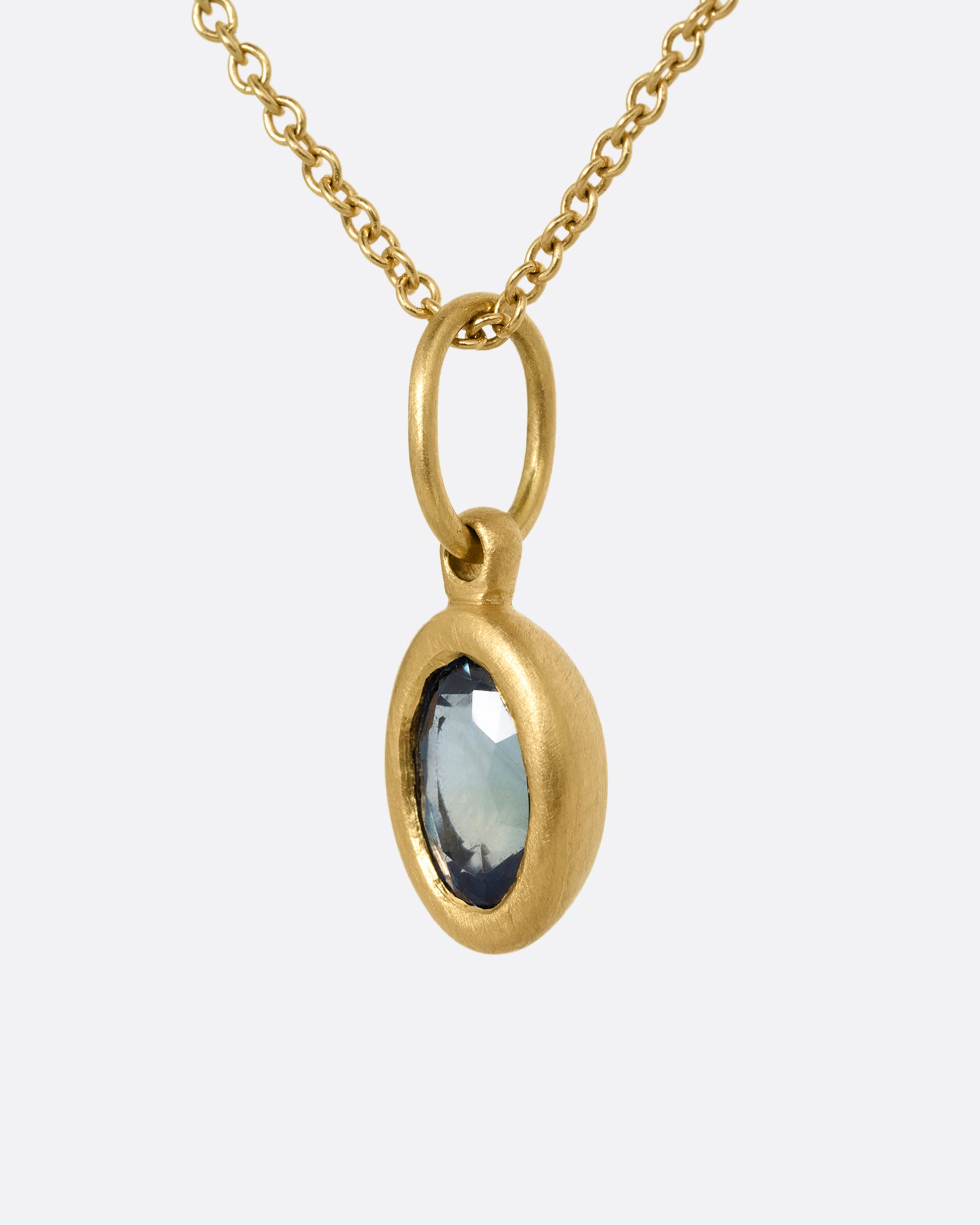 A yellow gold cable chain necklace with a bezel set oval blue green sapphire. Shown from the side.