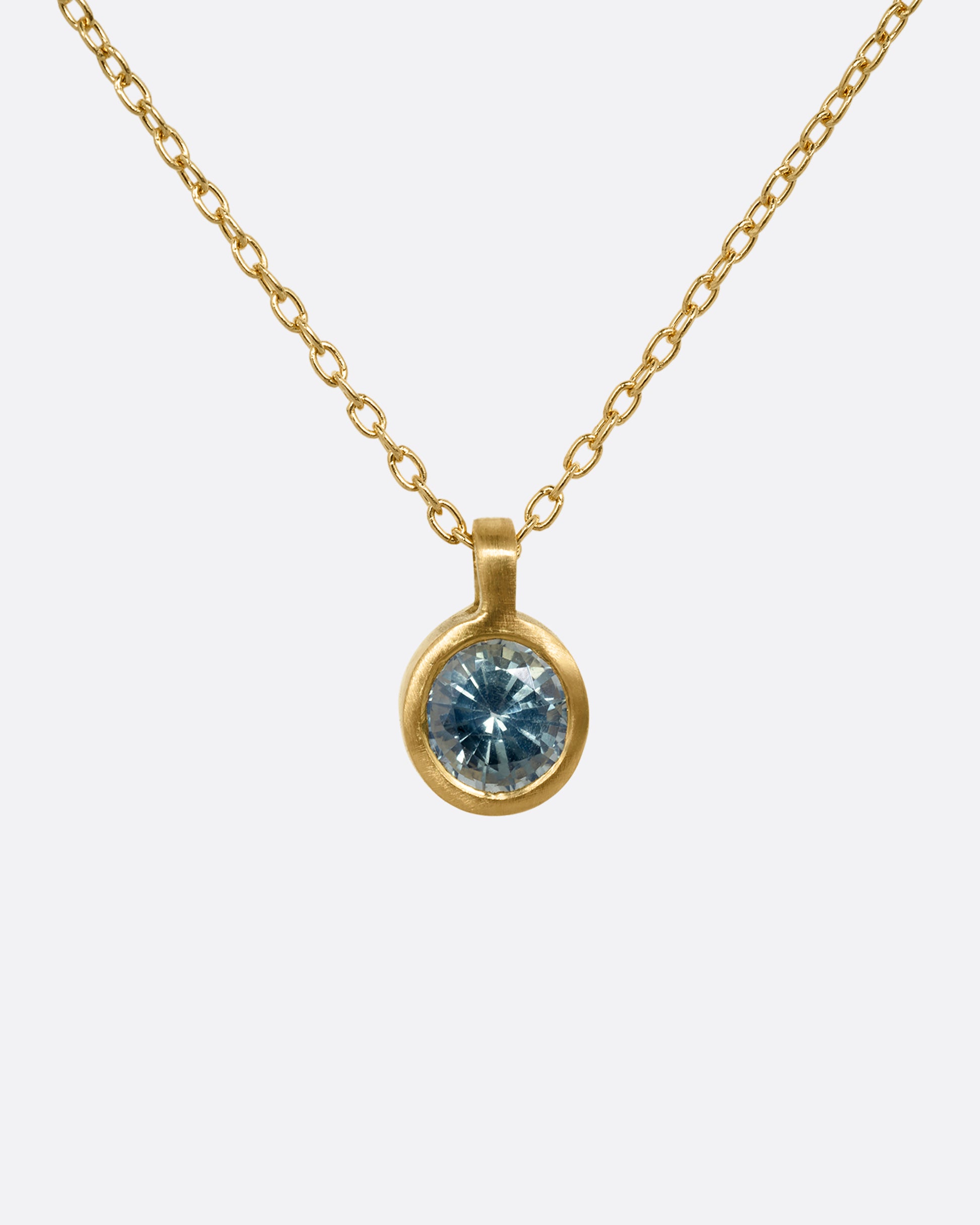 A yellow gold cable chain necklace with a round bezel set faceted blue green sapphire. Shown from the front.