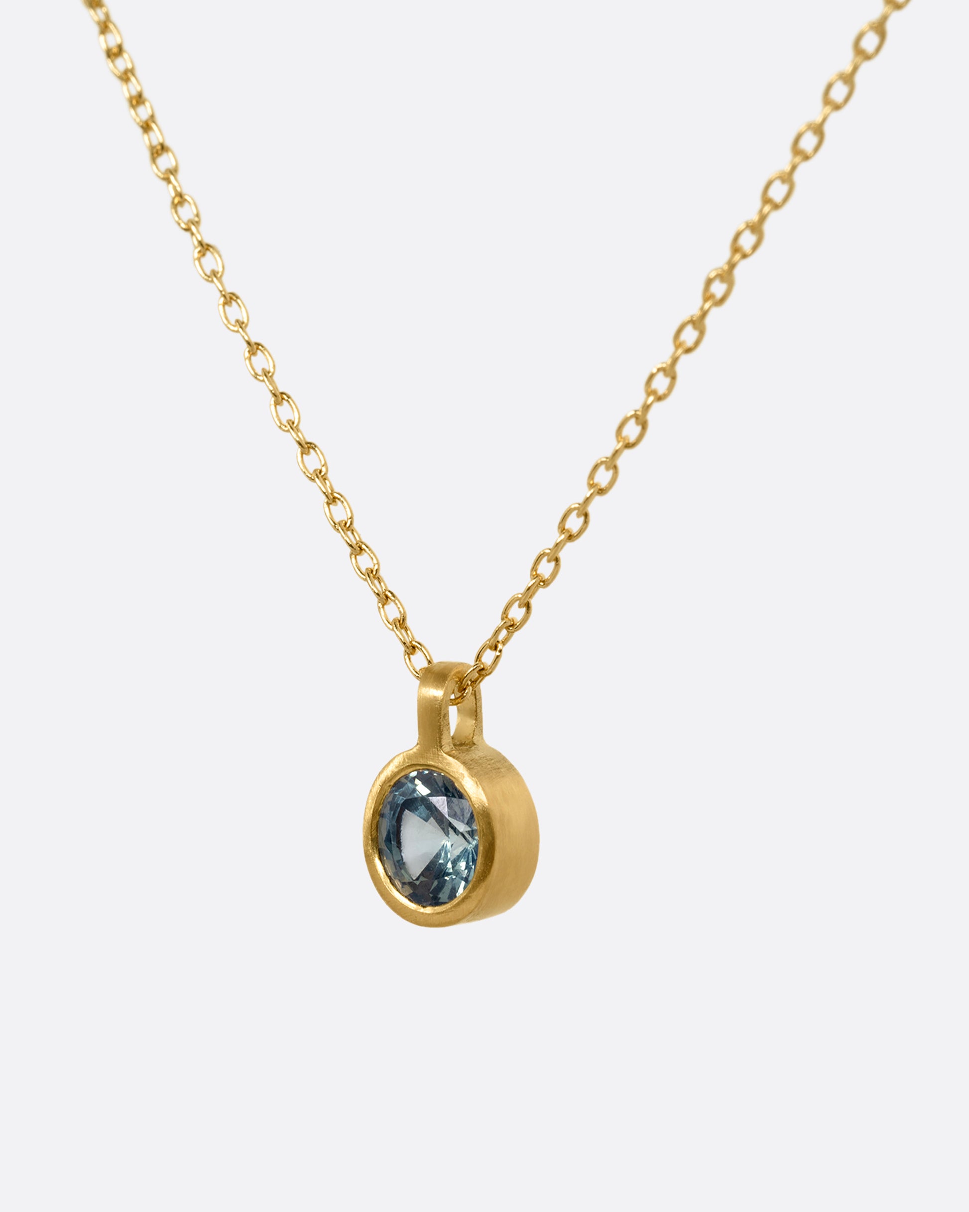 A yellow gold cable chain necklace with a round bezel set faceted blue green sapphire. Shown from the side.