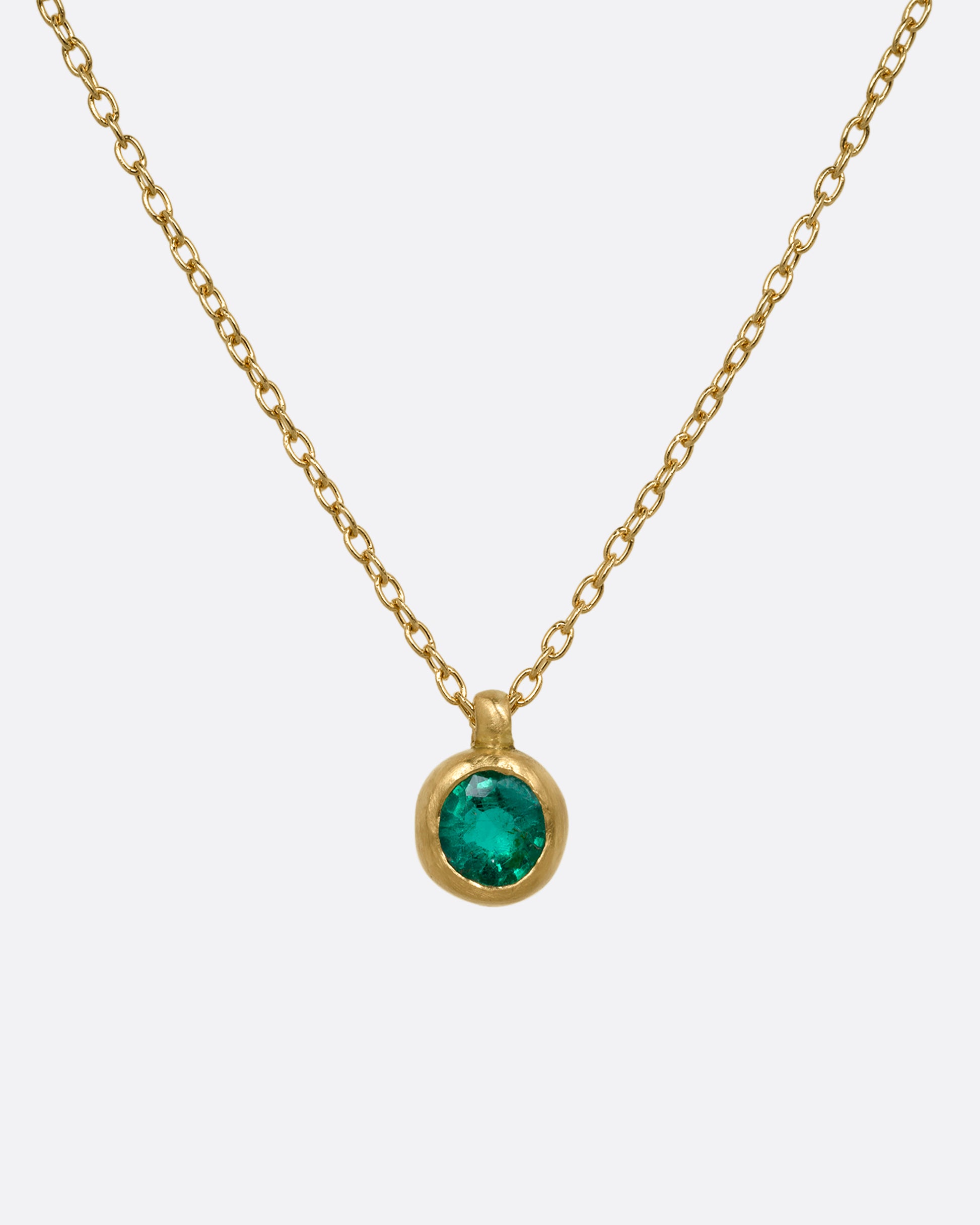 A yellow gold cable chain necklace with a faceted emerald in a satiny gold bezel. Shown from the front.
