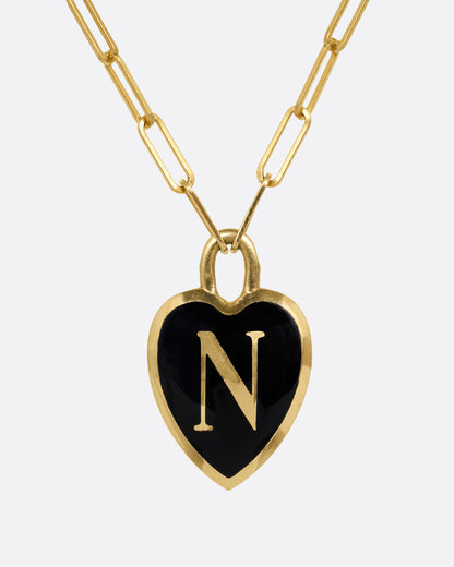 A yellow gold  paperclip chain necklace with a black enamel heart shaped N pendant. Shown from the front.