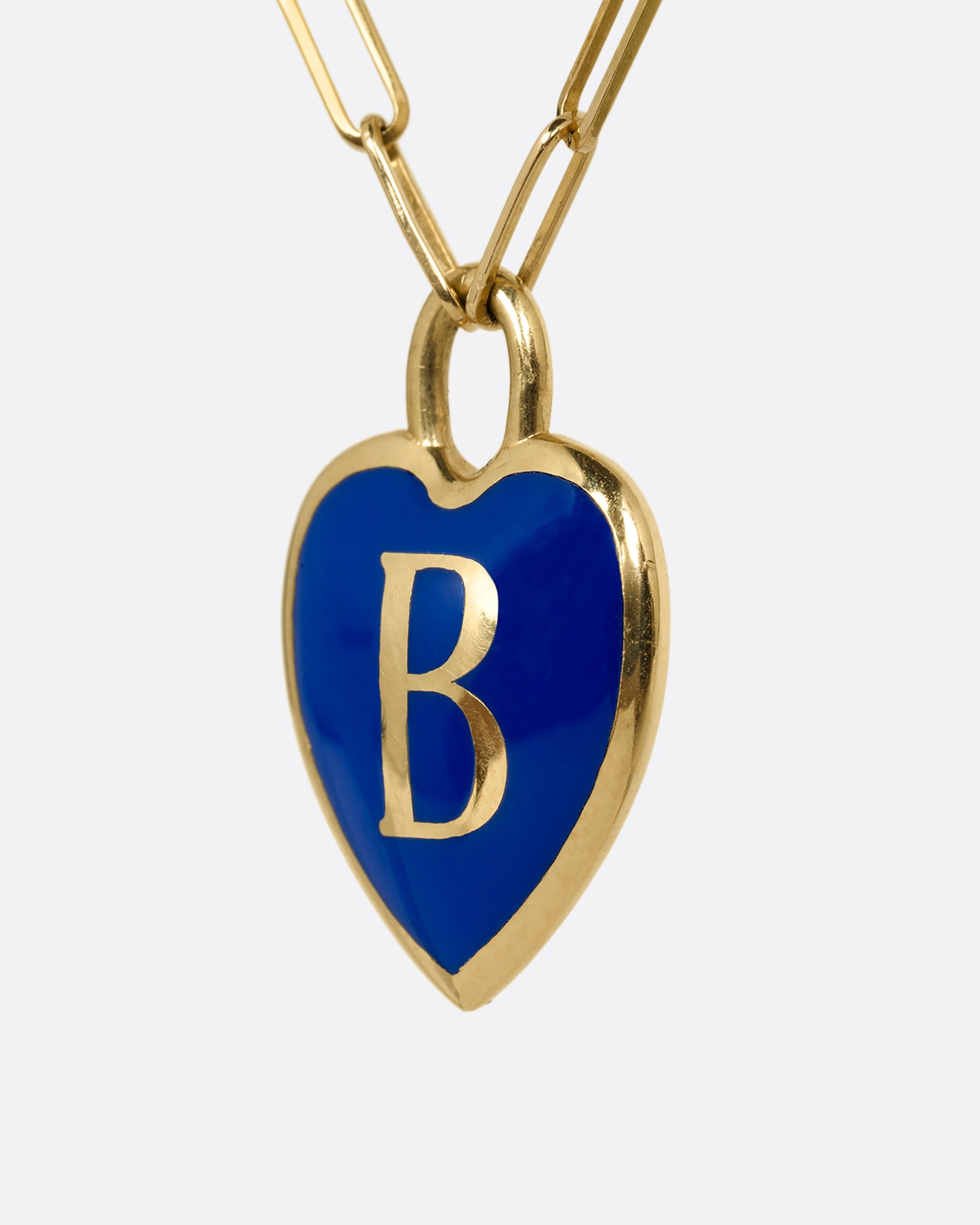 A yellow gold  paperclip chain necklace with a black enamel heart shaped N pendant. Shown from the side.