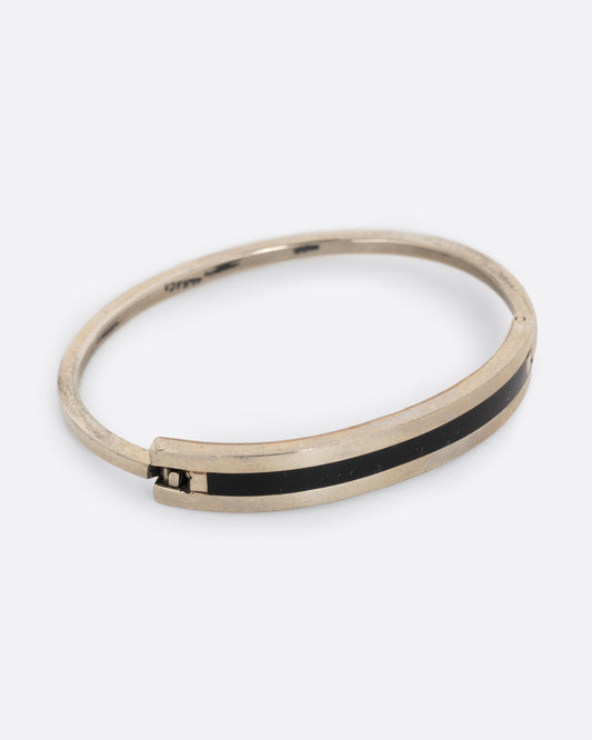 An alpaca silver bracelet with a black enamel stripe and hinged closure. Shown from the side.