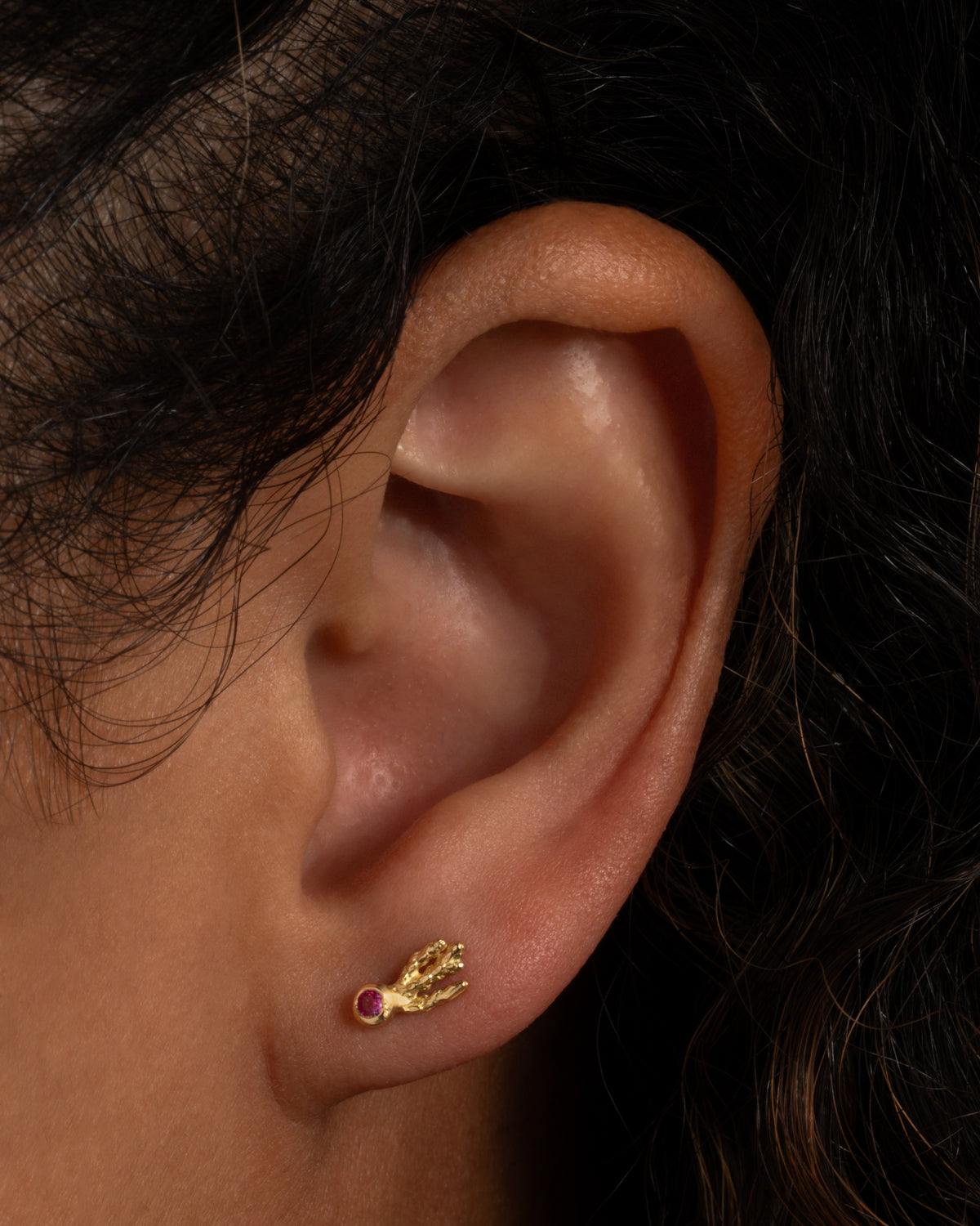 Yellow gold orange sapphire comet stud earrings worn on an ear