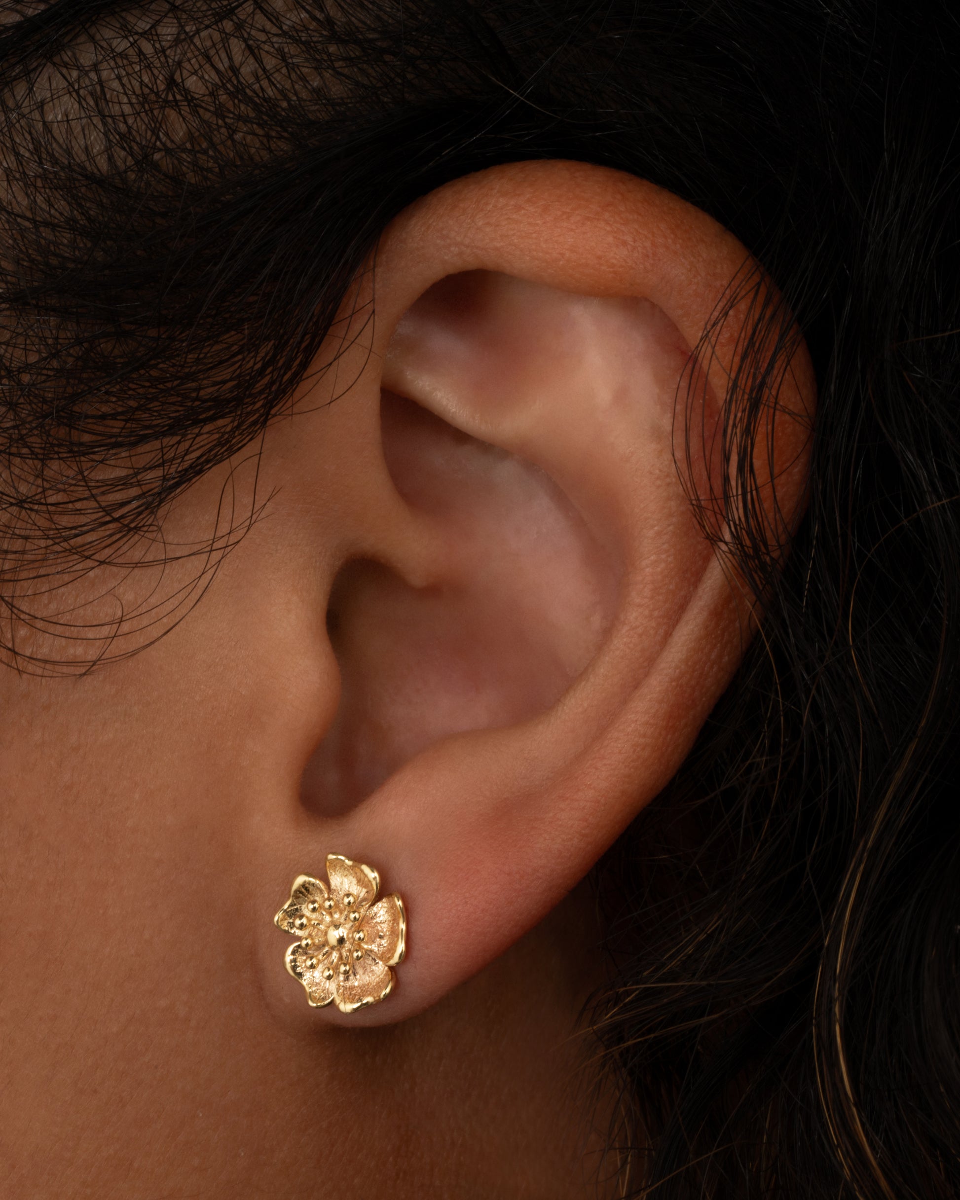 A yellow gold flower stud earring. Shown from the front on a person.
