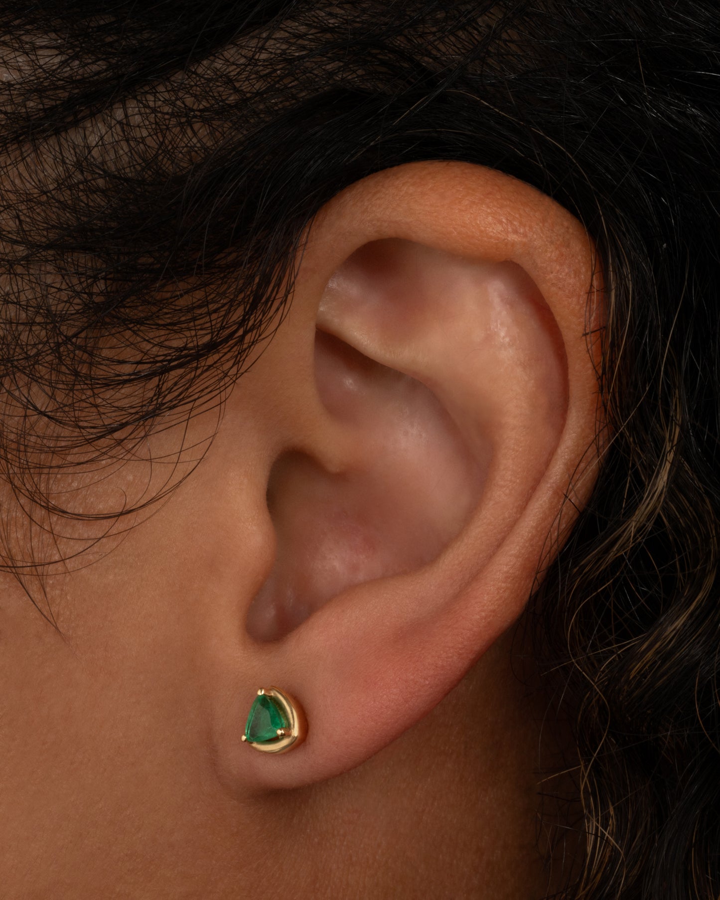 A yellow gold stud earring with an emerald. Shown on a person.