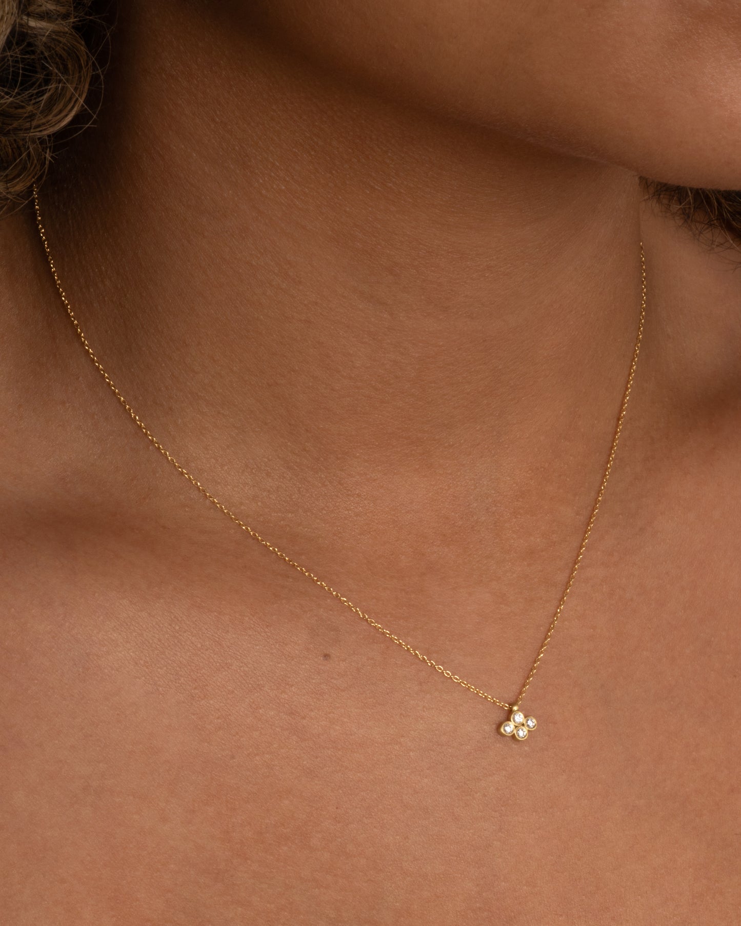 A yellow gold cable chain necklace with a pendant of four two point diamonds. Shown worn around the neck.