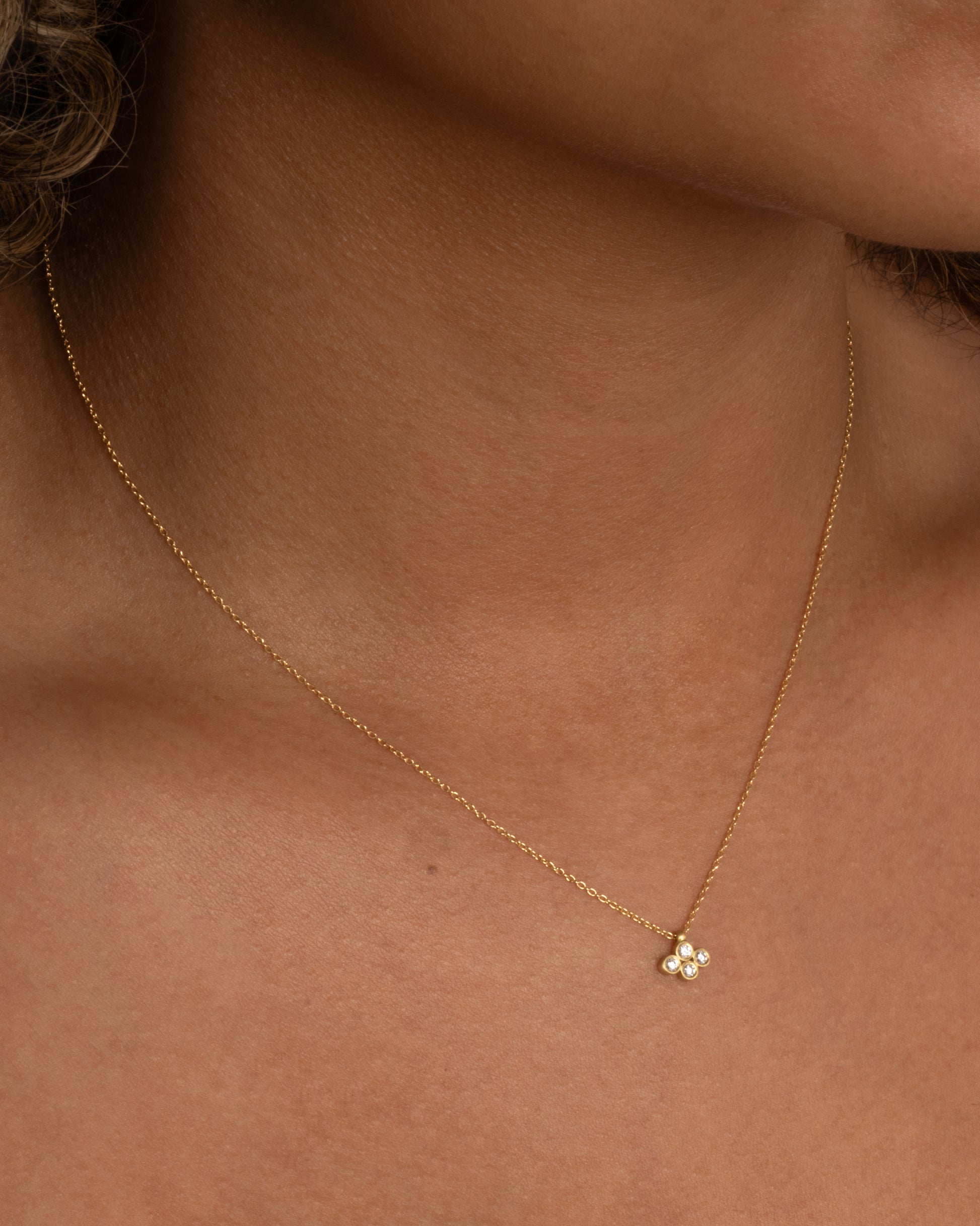 A yellow gold cable chain necklace with a pendant of four two point diamonds. Shown worn around the neck.
