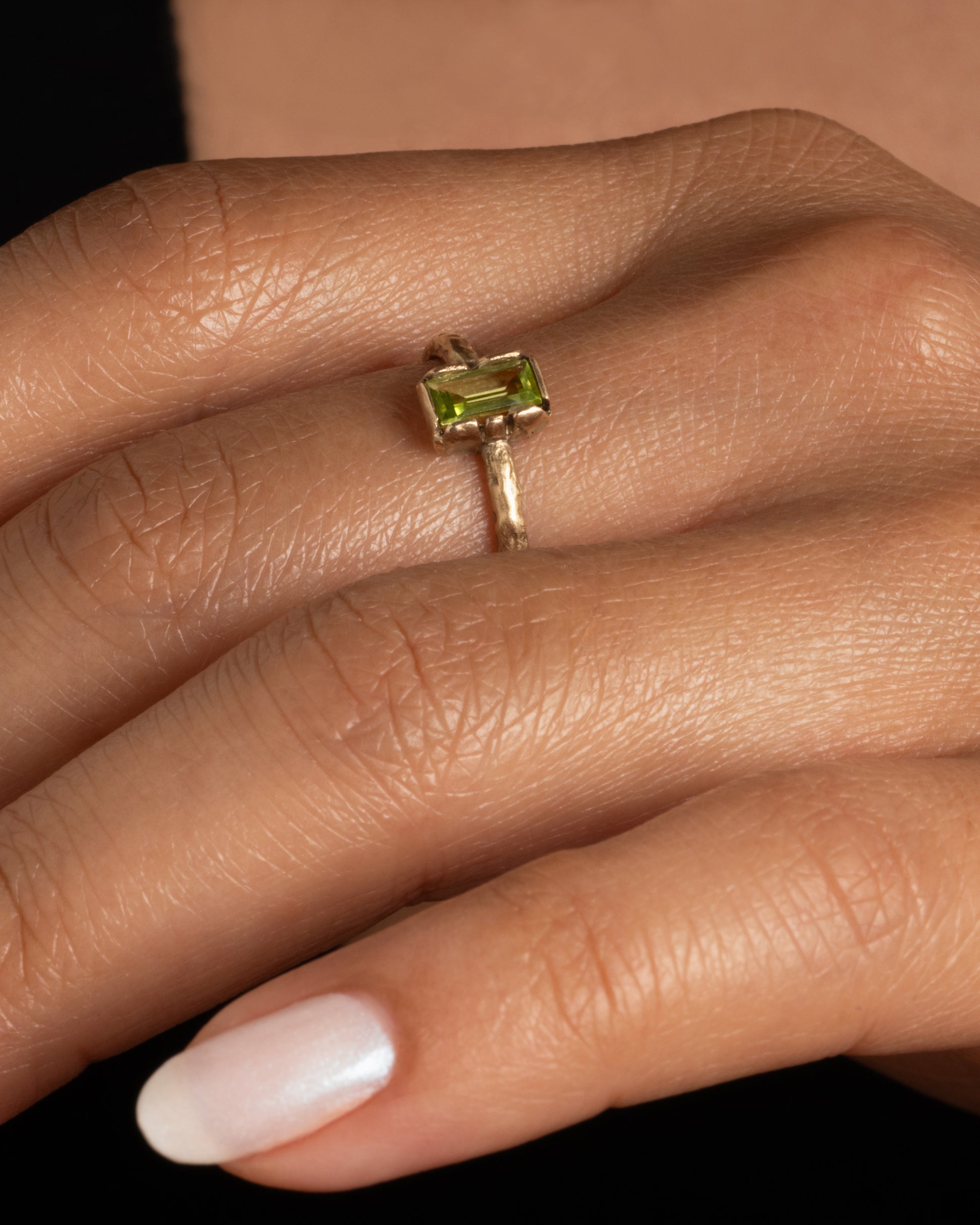 A textured yellow gold ring with a rectangular peridot. Shown worn on a finger.