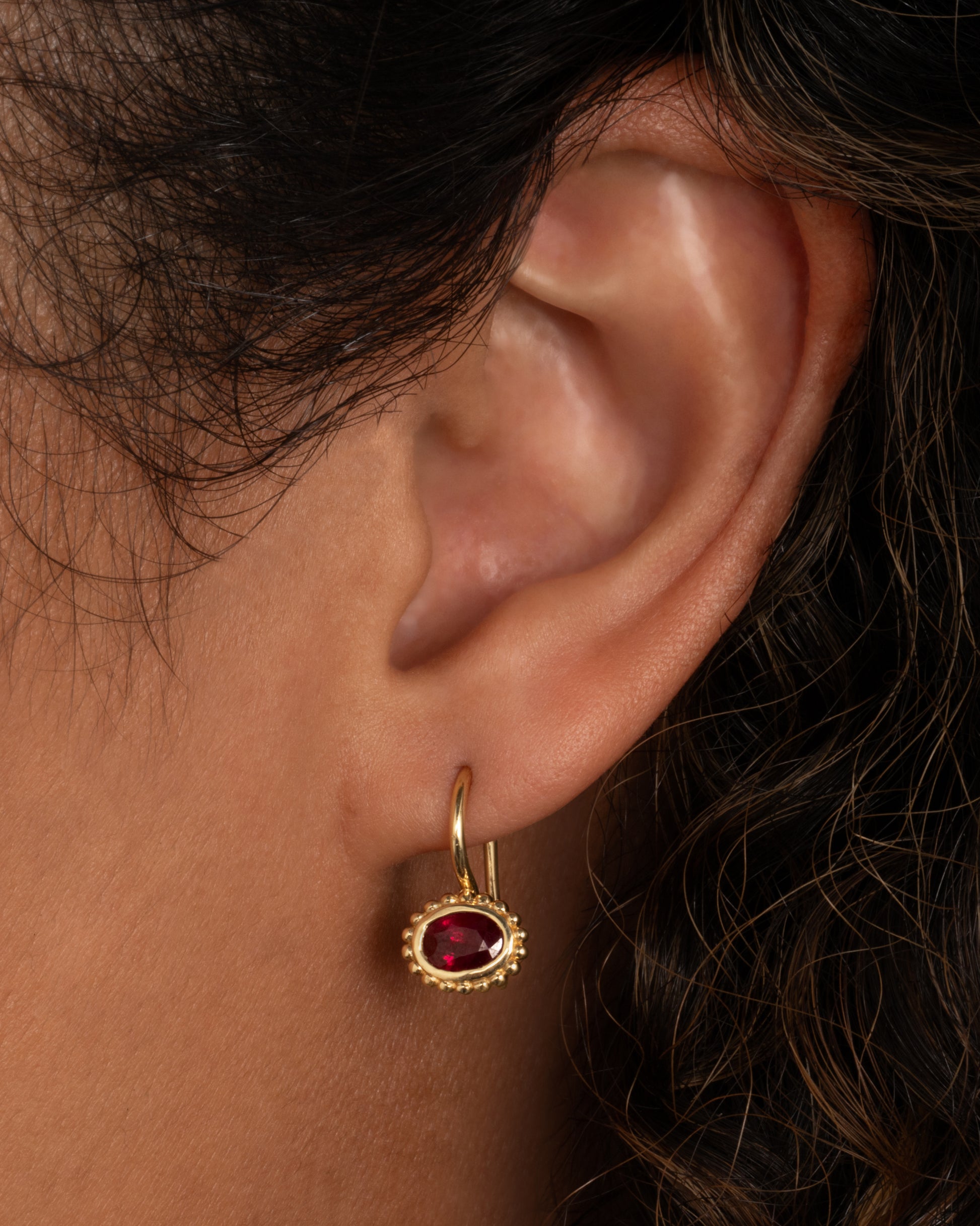yellow gold ruby earrings shown worn in an ear.