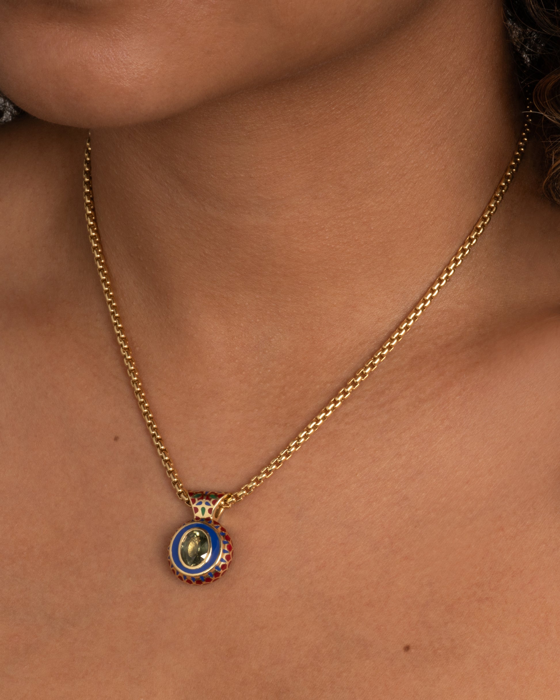 yellow gold green sapphire pendant with enamel shown worn around a neck