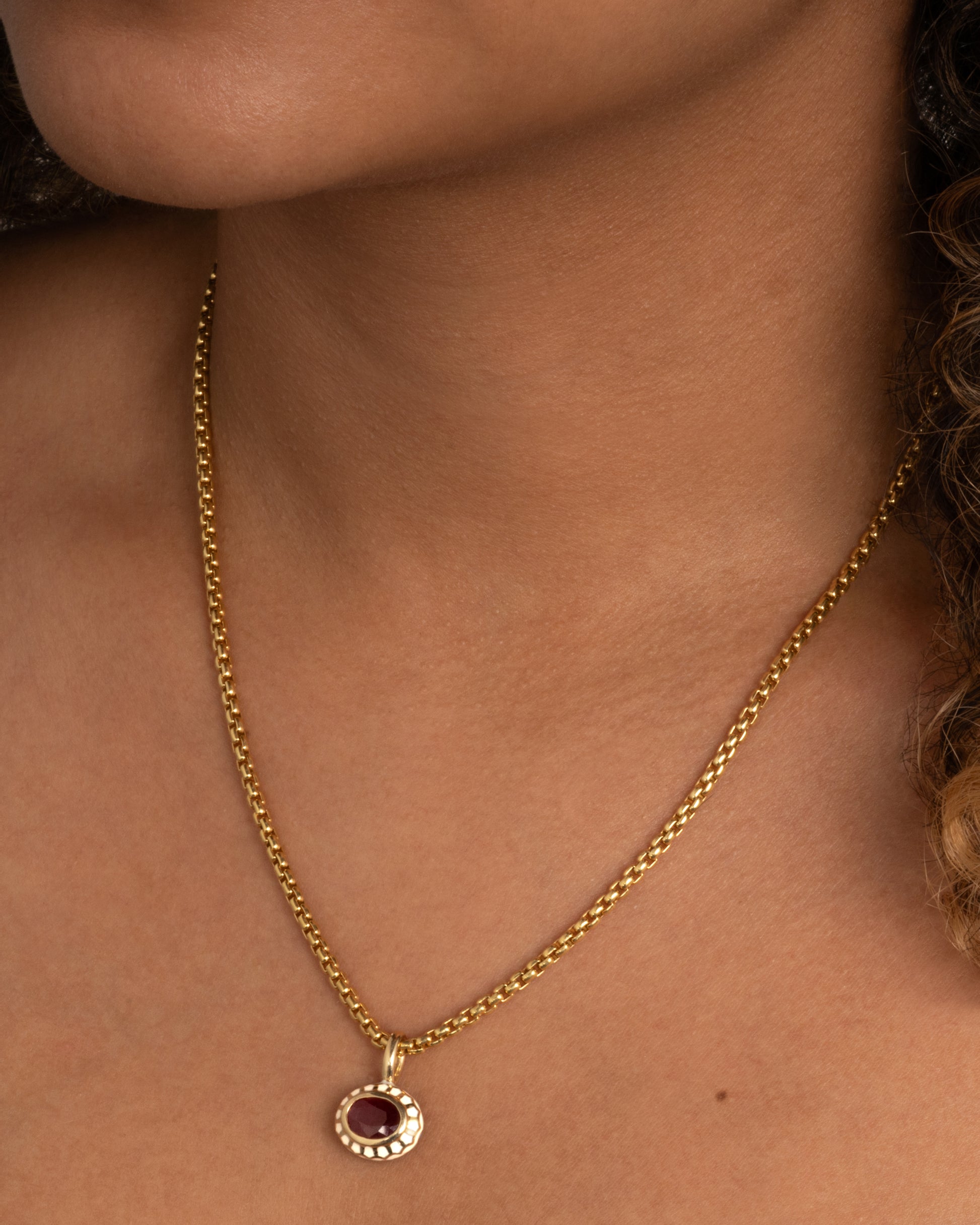 yellow gold ruby pendant with enamel shown worn around the neck