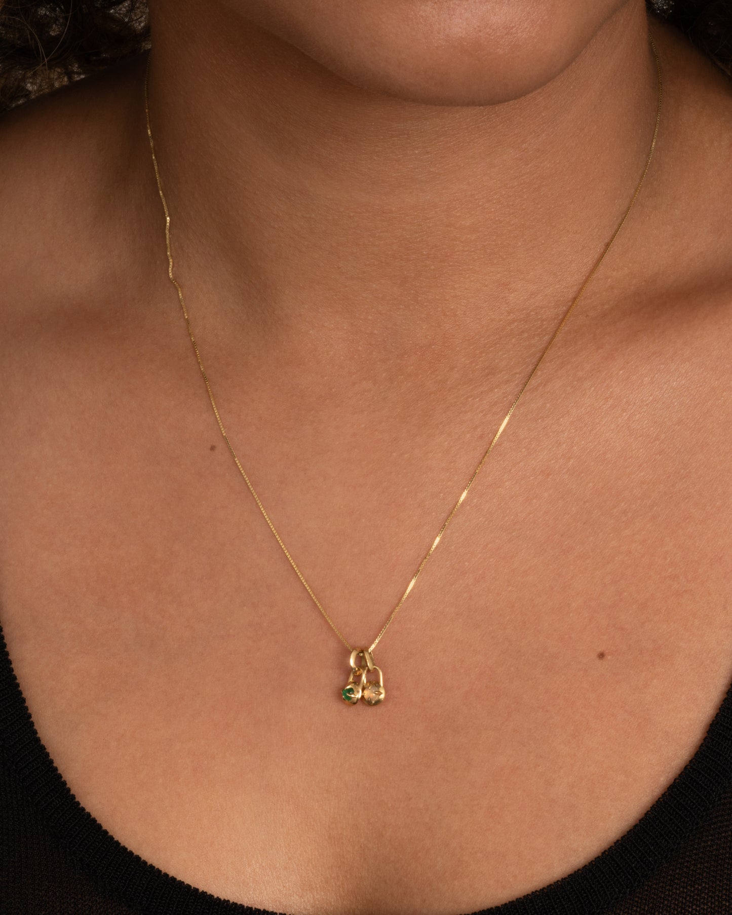 A yellow gold necklace with two pendants, one with an emerald and one with an opal, shown on a person.