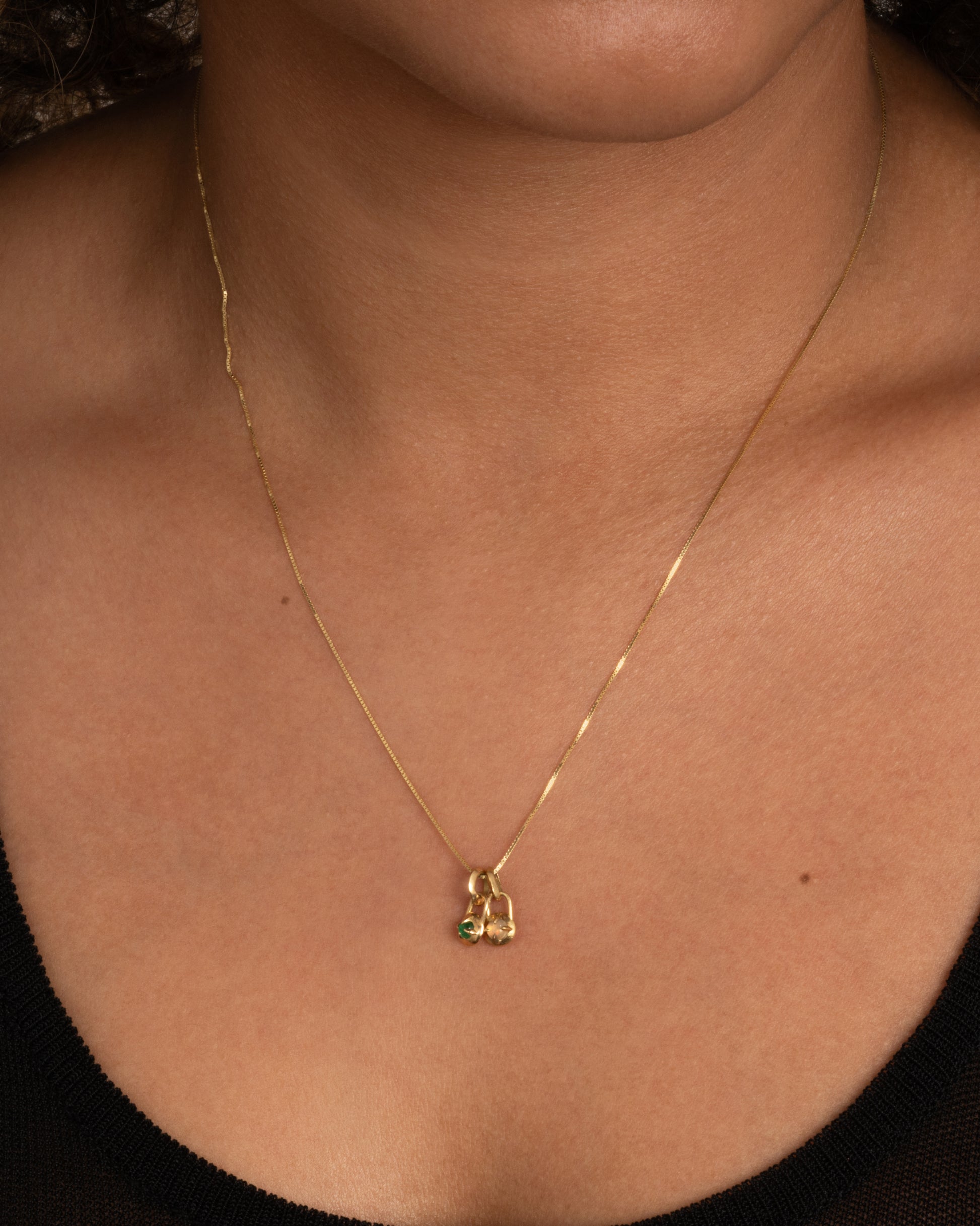 A yellow gold necklace with two pendants, one with an emerald and one with an opal, shown on a person.