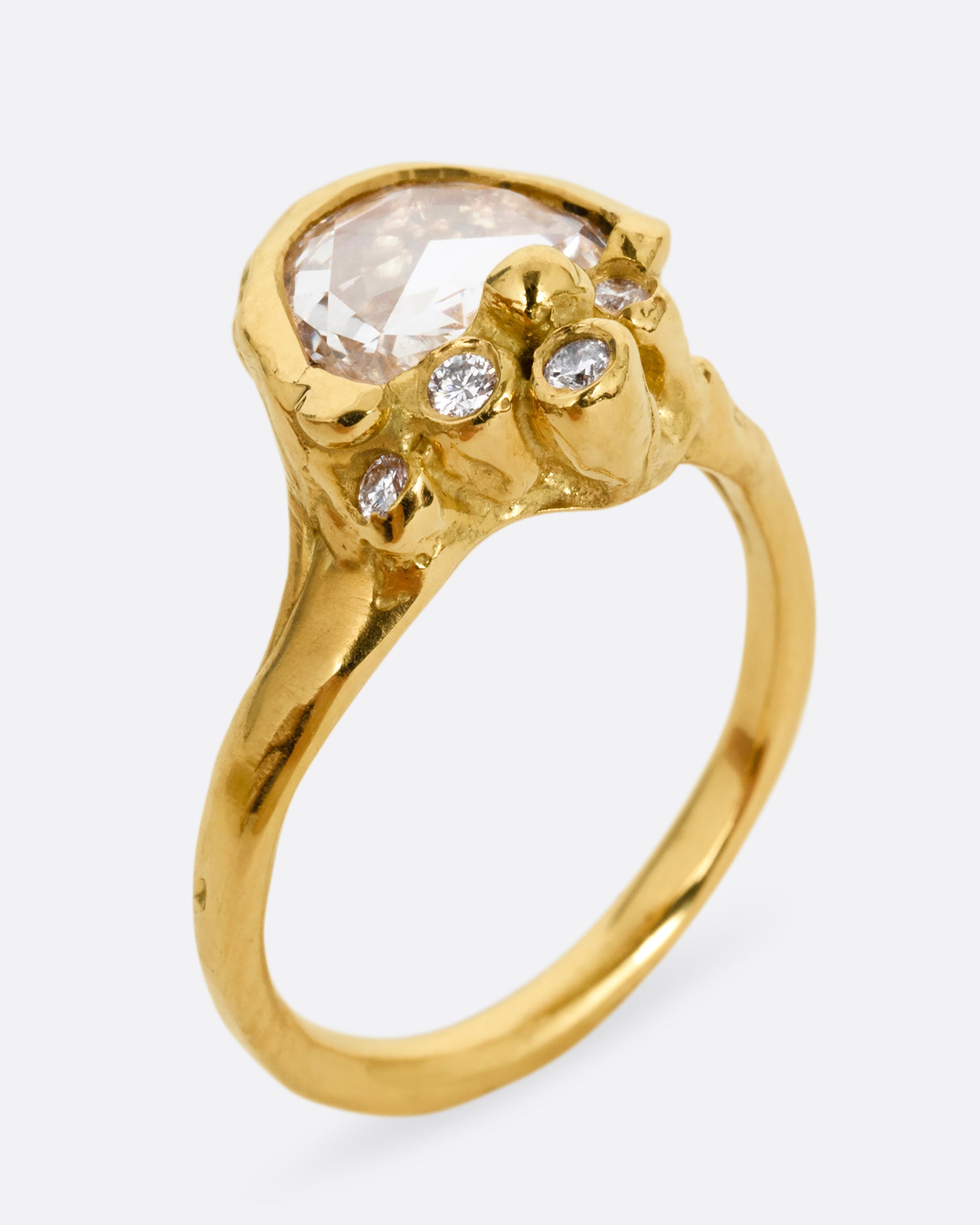 A yellow gold ring with  a central rose cut diamond half moon and bezel set diamond accents on top of the flat side. Shown from the side at an angle. 
