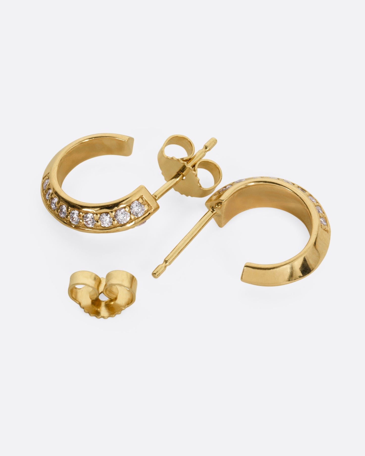 A pair of yellow gold hoop earrings with diamonds, shown from the side with one hoop open.