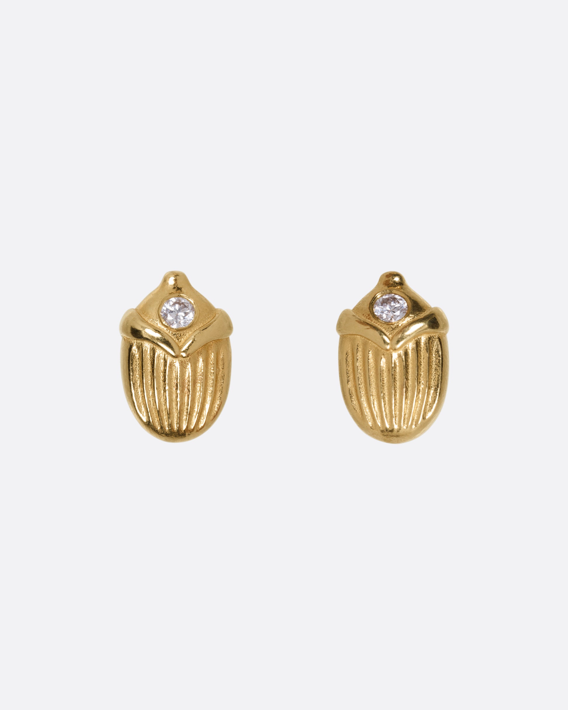 A pair of yellow gold scarab shaped stud earrings, each punctuated by a diamond, shown from the front.