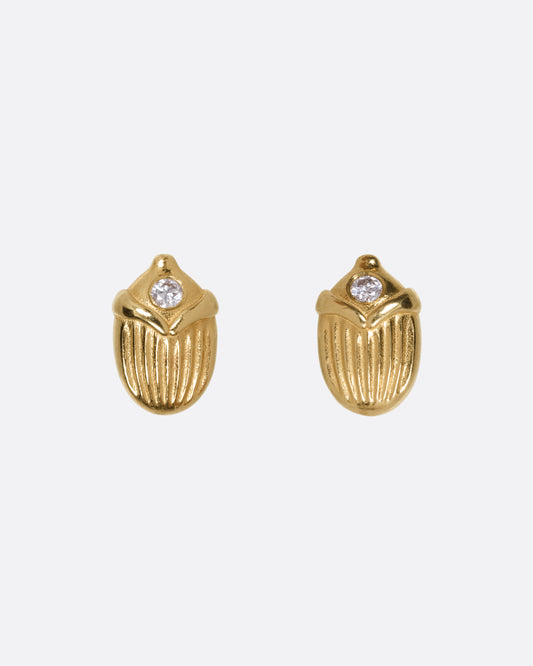 A pair of yellow gold scarab shaped stud earrings, each punctuated by a diamond, shown from the front.