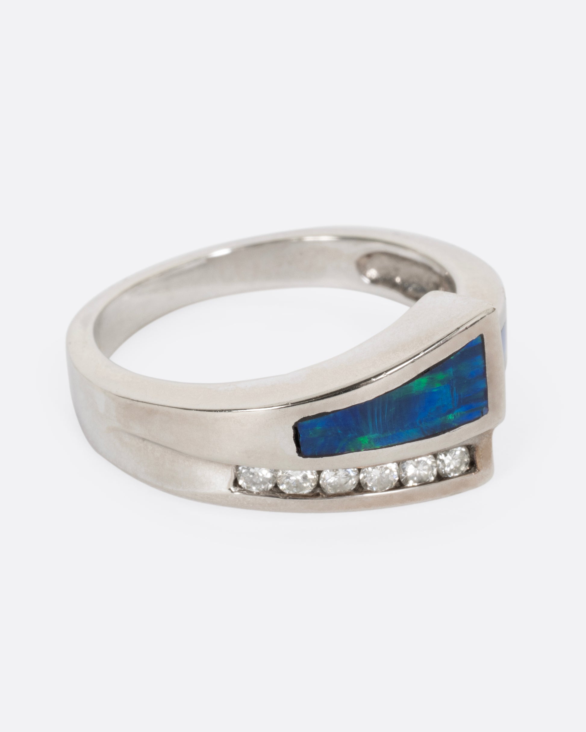 A white gold wrap ring with opal inlay and  a queue of diamonds along the edge, shown from the side.