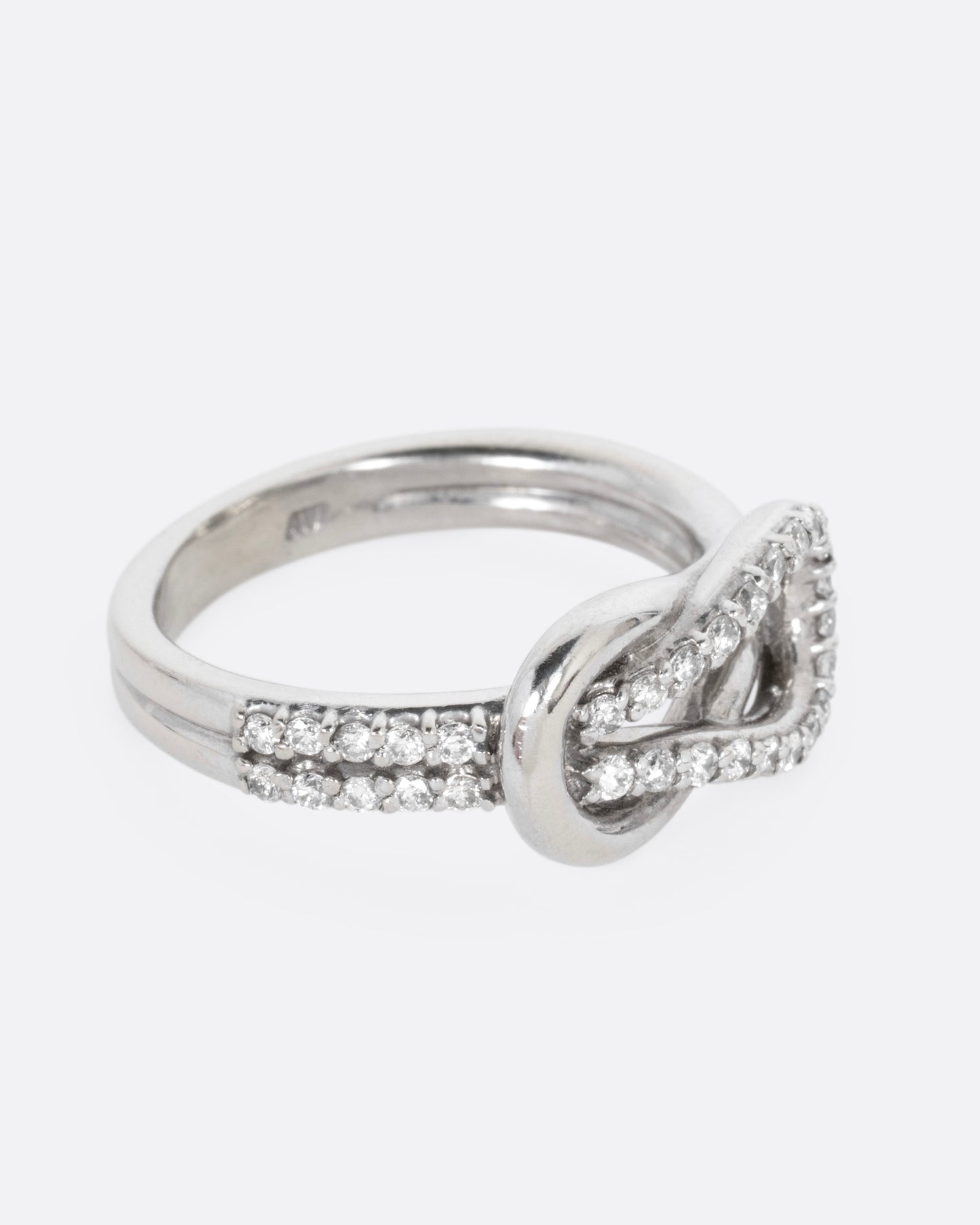 A white gold ring with a diamond studded infinity knot, shown from the side.