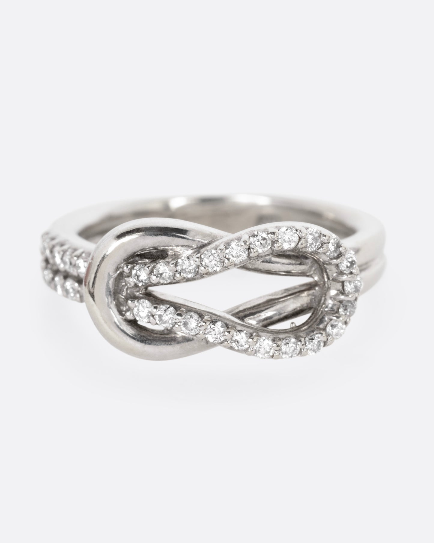 A white gold ring with a diamond studded infinity knot, shown from the front.