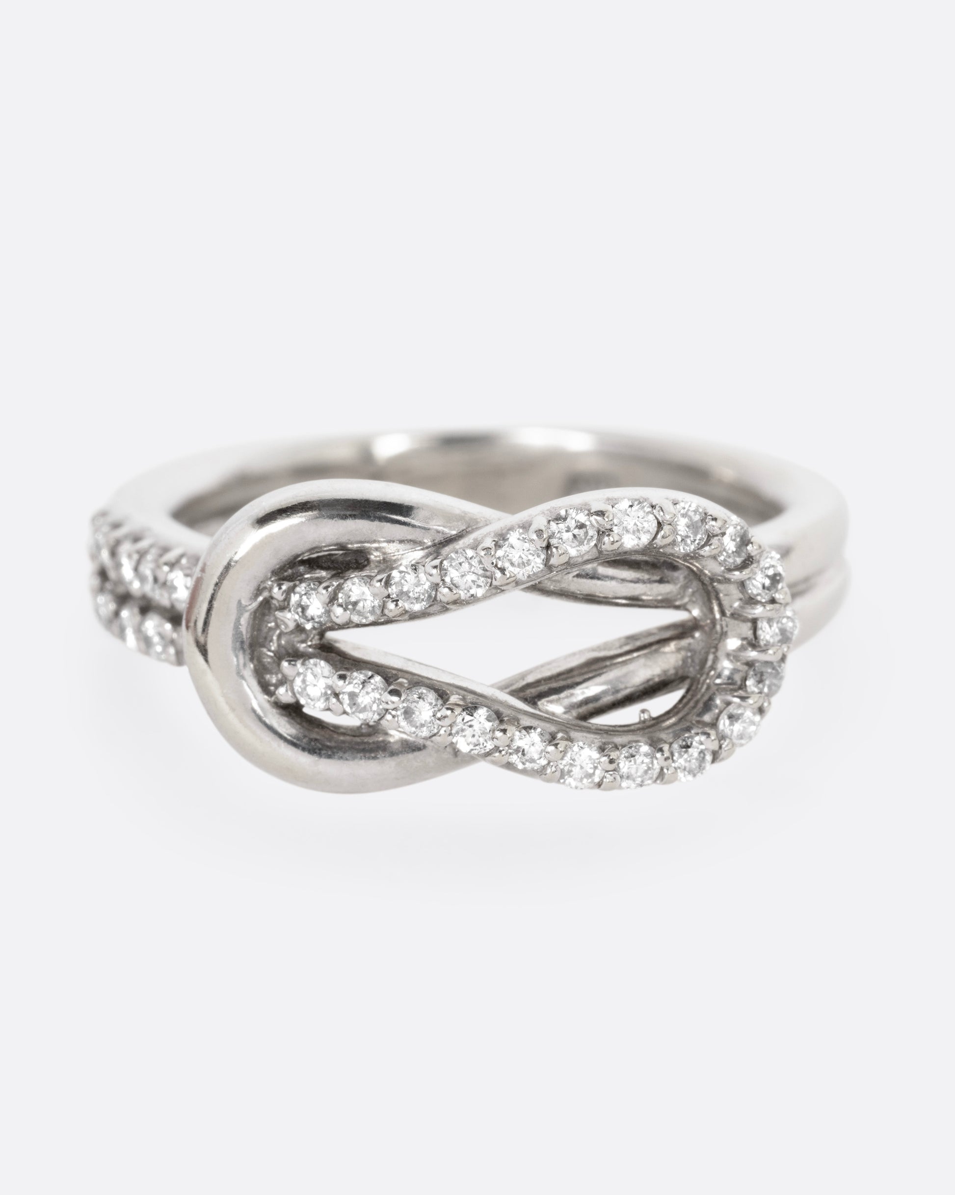 A white gold ring with a diamond studded infinity knot, shown from the front.