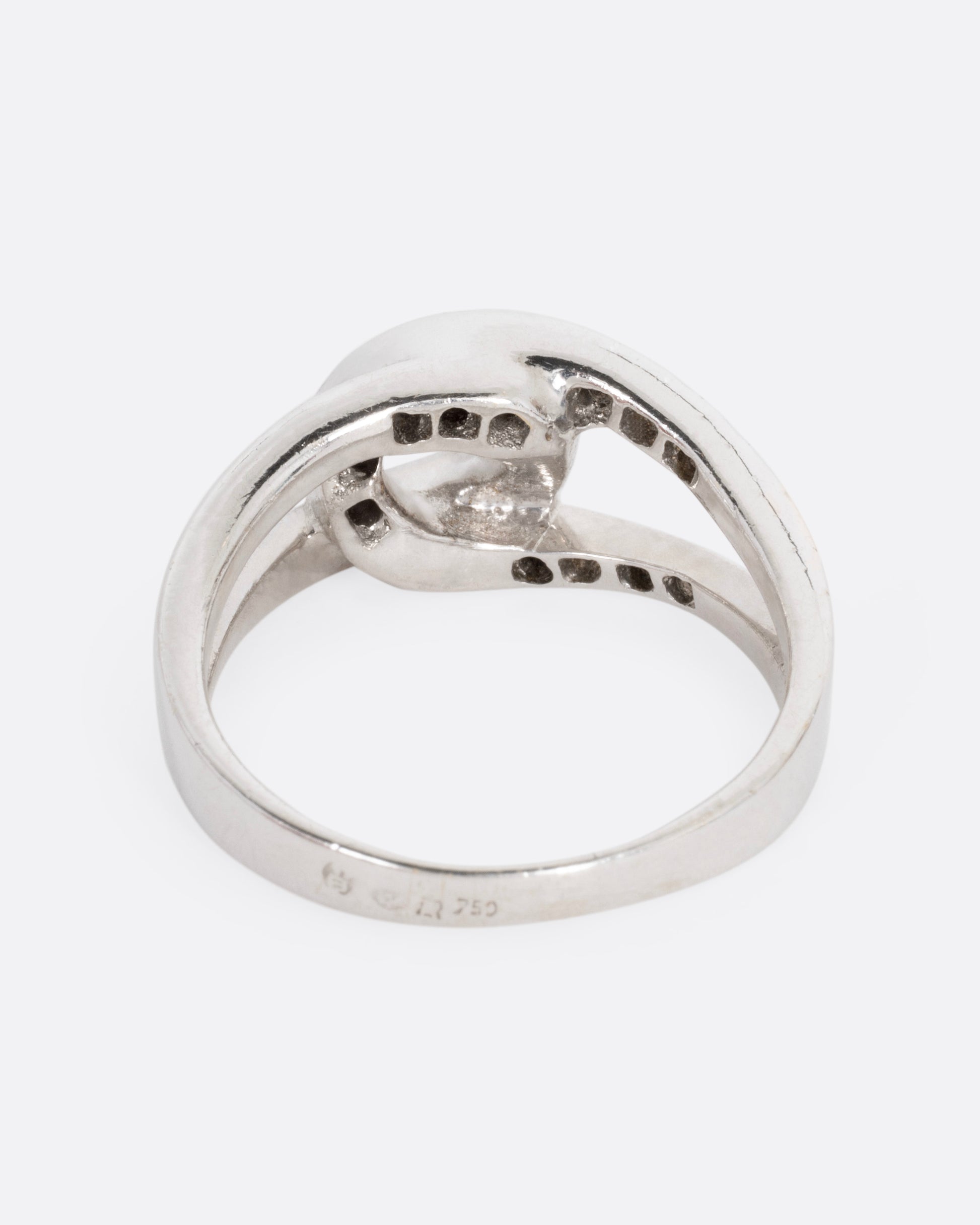 A white gold ring with two interlocking loops; one studded with diamonds, shown from the back.
