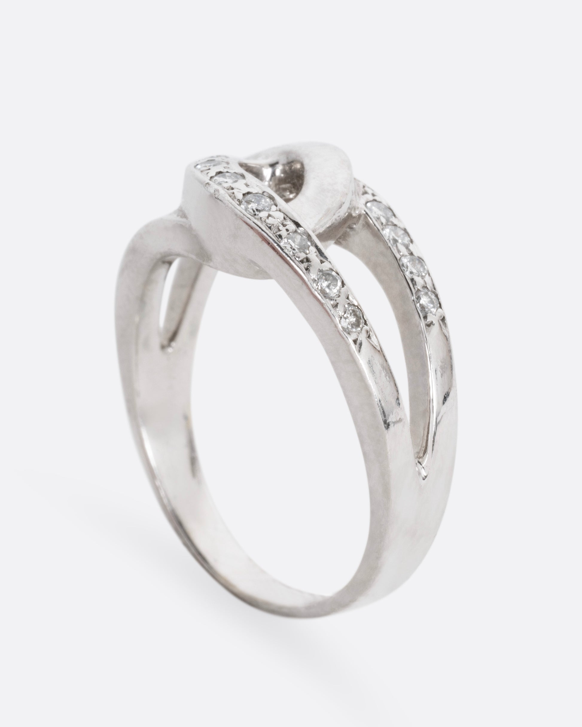 A white gold ring with two interlocking loops; one studded with diamonds, shown from the side standing up.