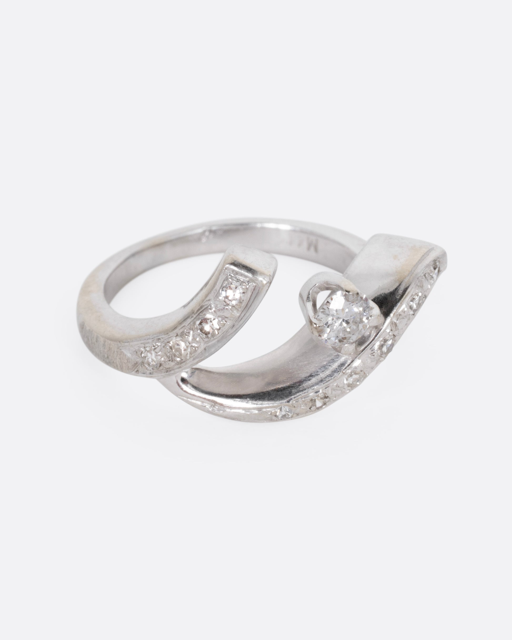 A white gold ring with a curving freeform silhouette, bead set diamonds, and a brilliant cut prong set central diamond, shown from the side.