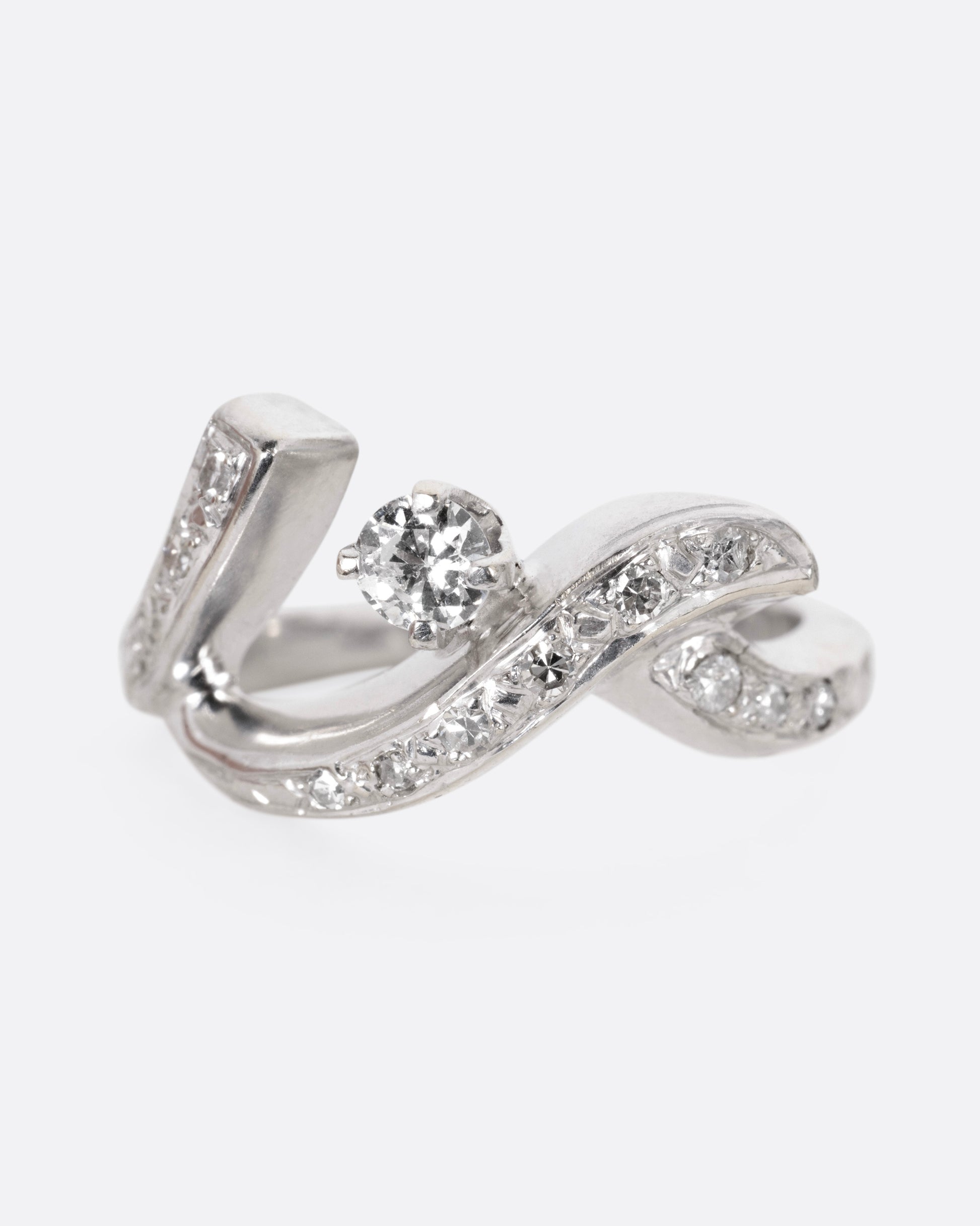 A white gold ring with a curving freeform silhouette, bead set diamonds, and a brilliant cut prong set central diamond, shown from the front.