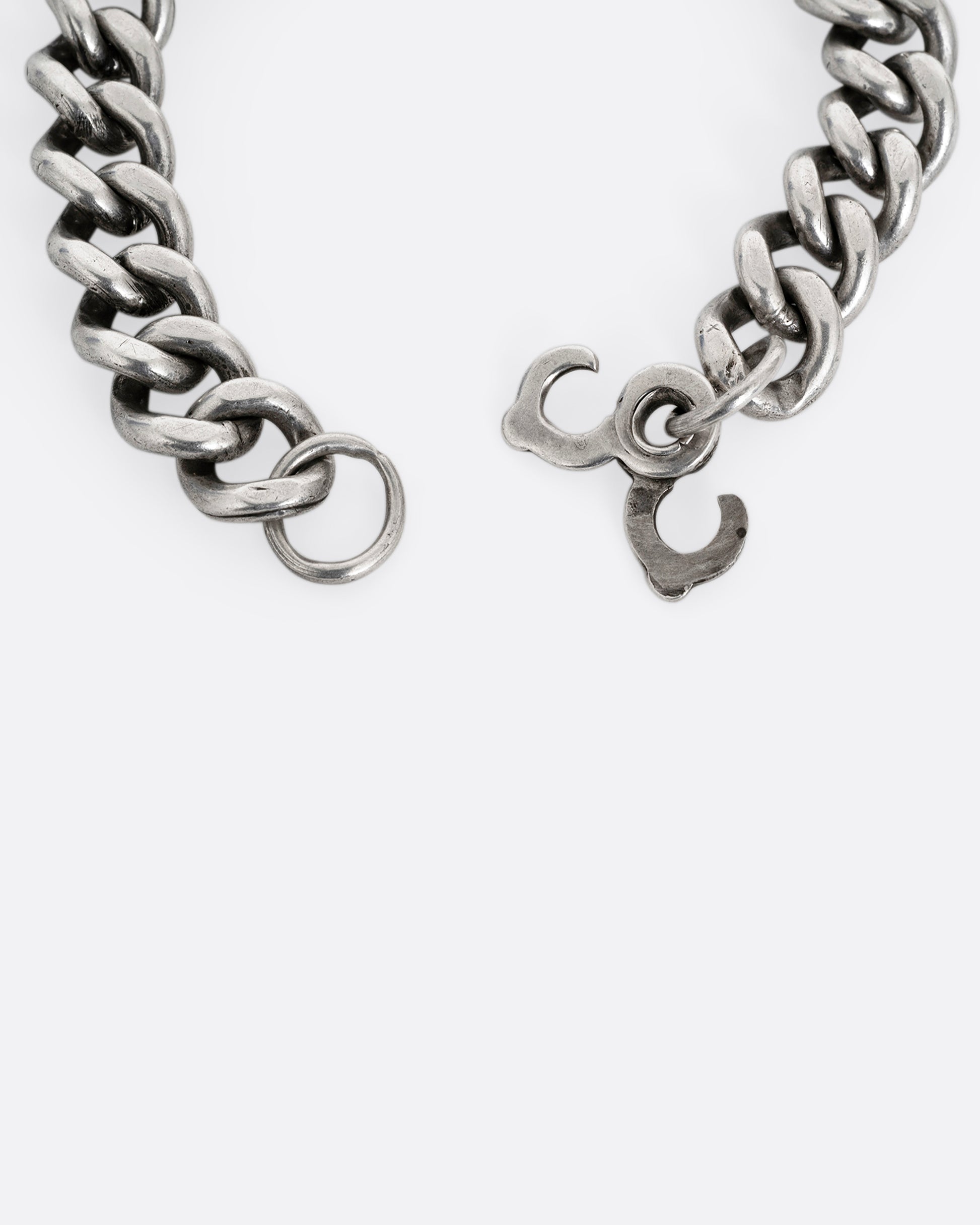 A close up of the clasp of a silver curb chain ID bracelet, shown from the back open.