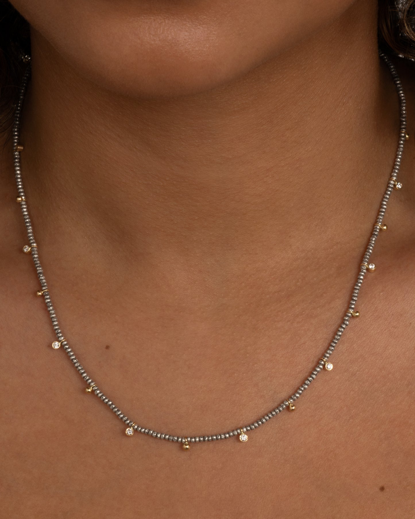 A necklace with nine brilliant cut diamond charms and ten gold drops among oxidized silver beads. Shown from the front on a person.