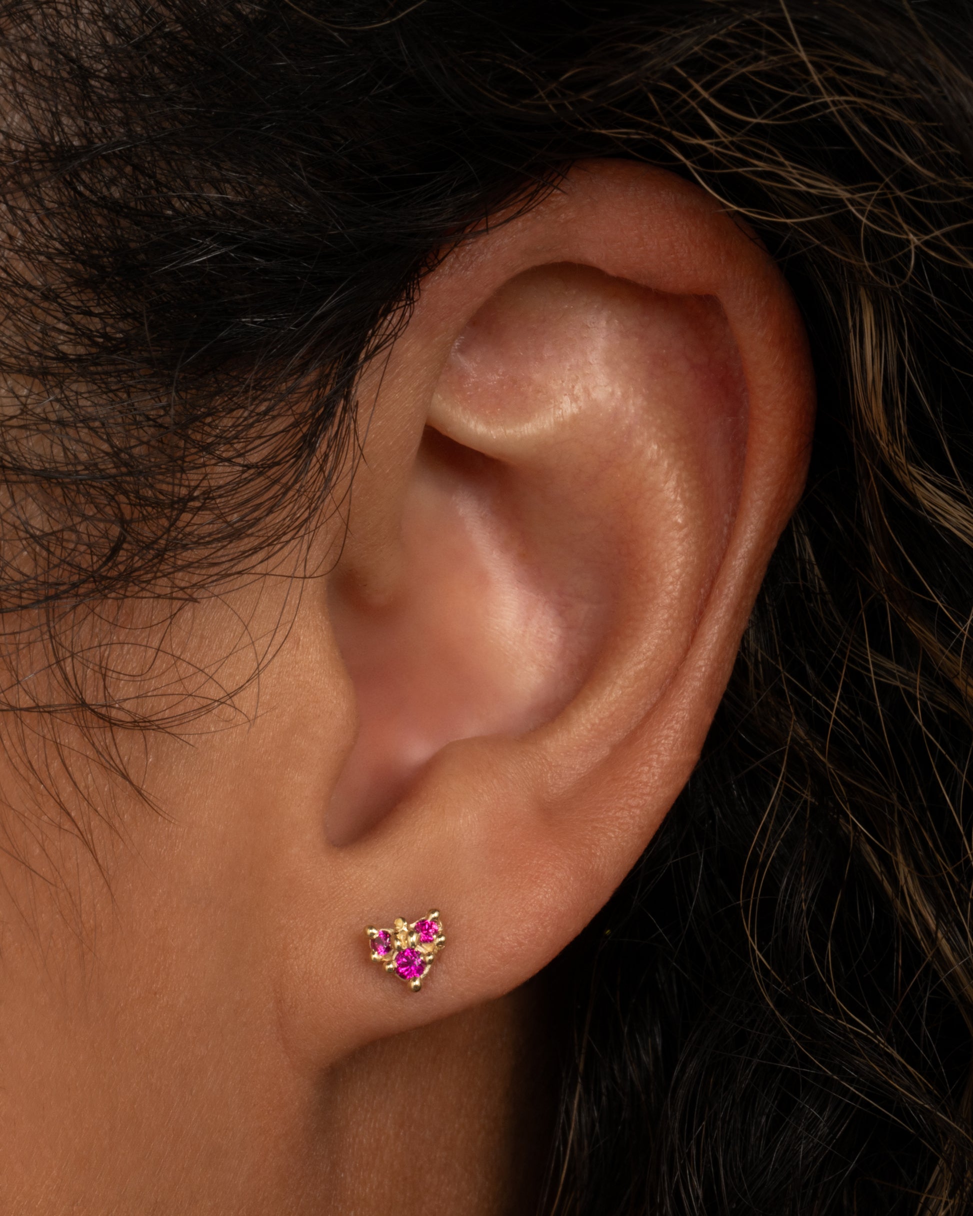 A textured arrow earring with three rosy rubies. Shown worn in an ear.