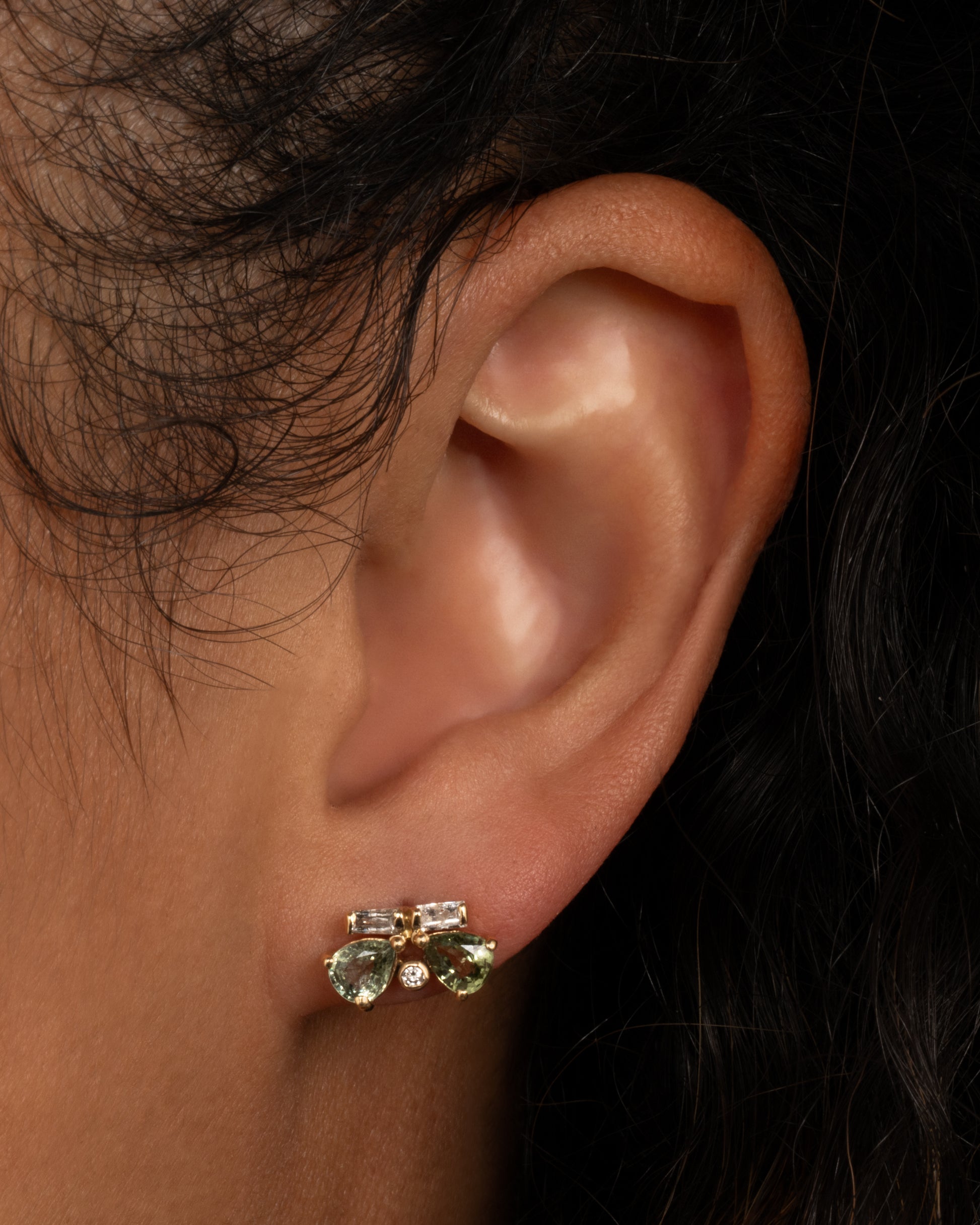A yellow gold earring in the shape of a butterfly with diamonds and sapphires. Shown worn in an ear.