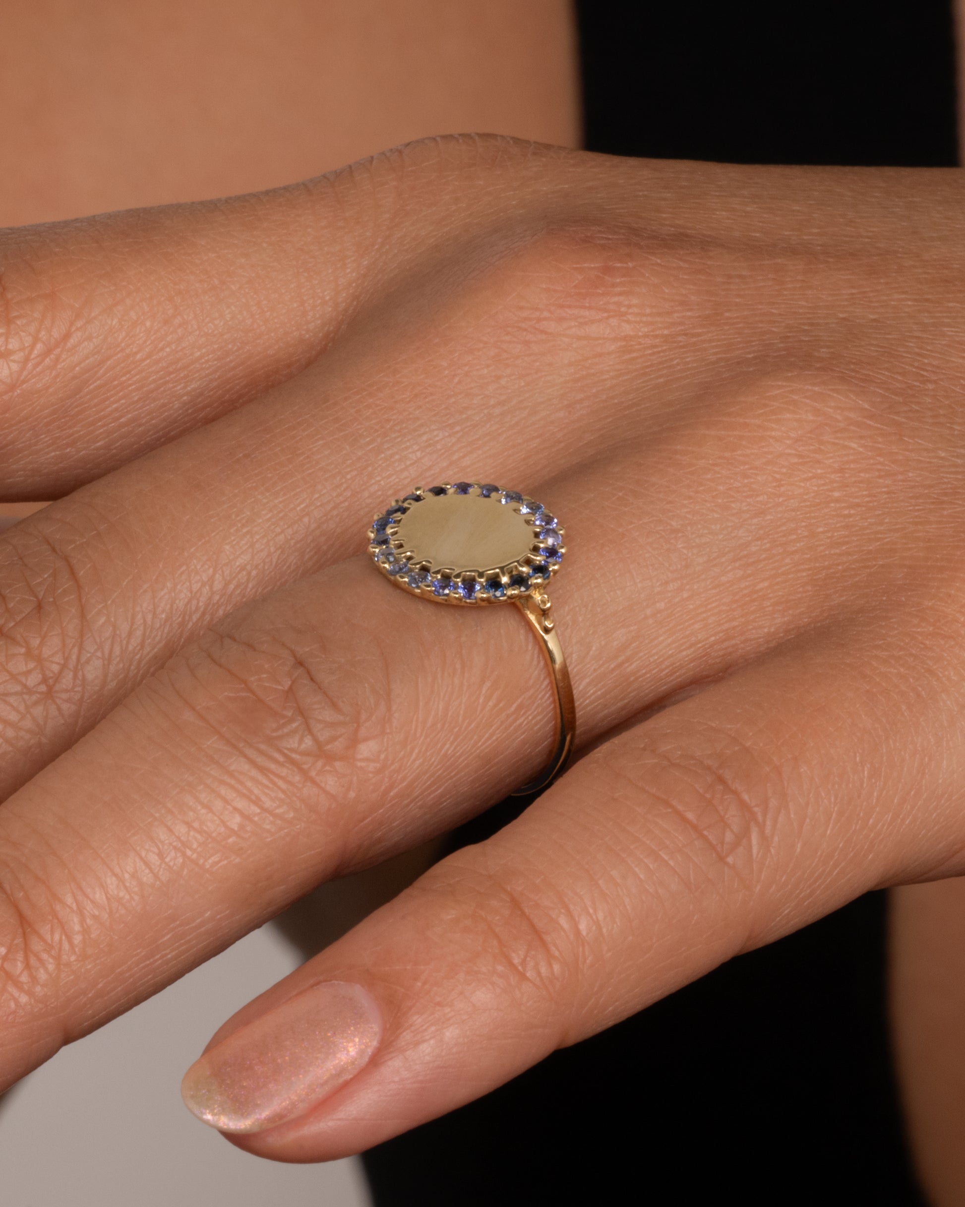 A 14k gold circle ring with a halo of ombré blue sapphires. Shown worn on hand.
