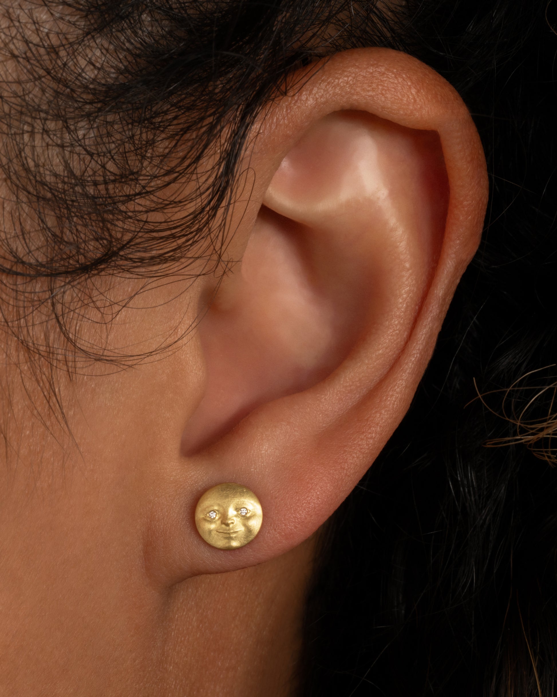 A yellow gold moon face stud earring with diamond eyes. Shown from the front on a person.