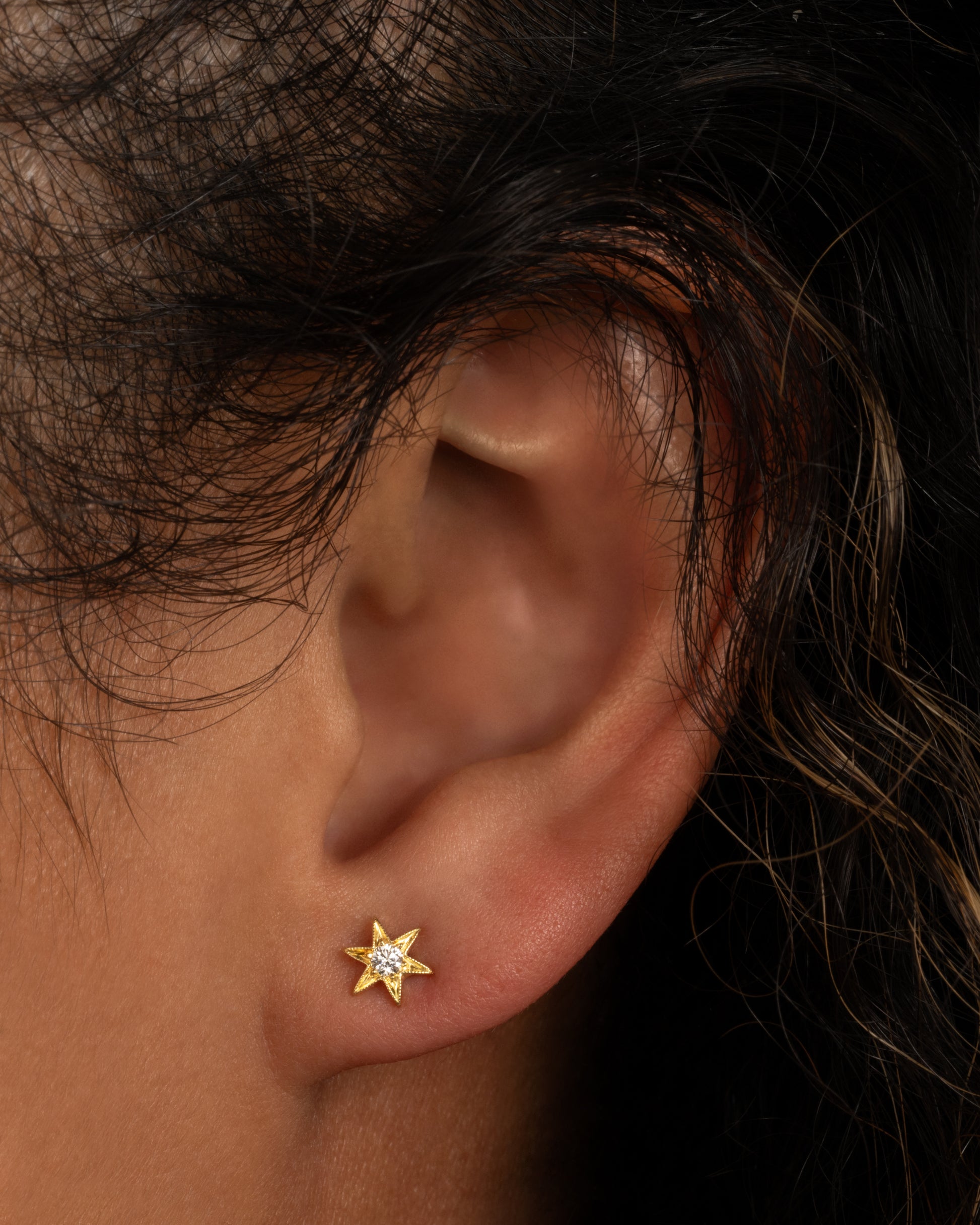 Yellow gold star stud earring with six points and millgrain details. Shown worn in an ear.