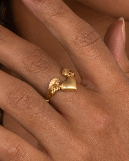 A yellow gold ring with a heart with wings on it. Shown worn on hand.
