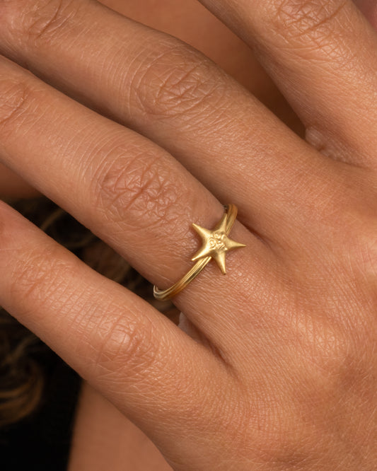 An 18k gold star ring with a sweet face emerging in the center. Shown worn on hand.
