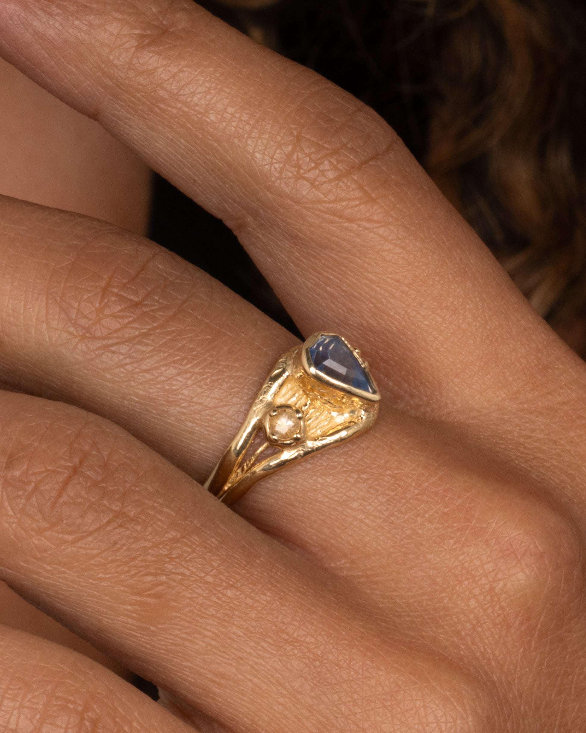 A yellow gold ring with a blue kite shaped sapphire and two yellow sapphires. Shown worn on finger.