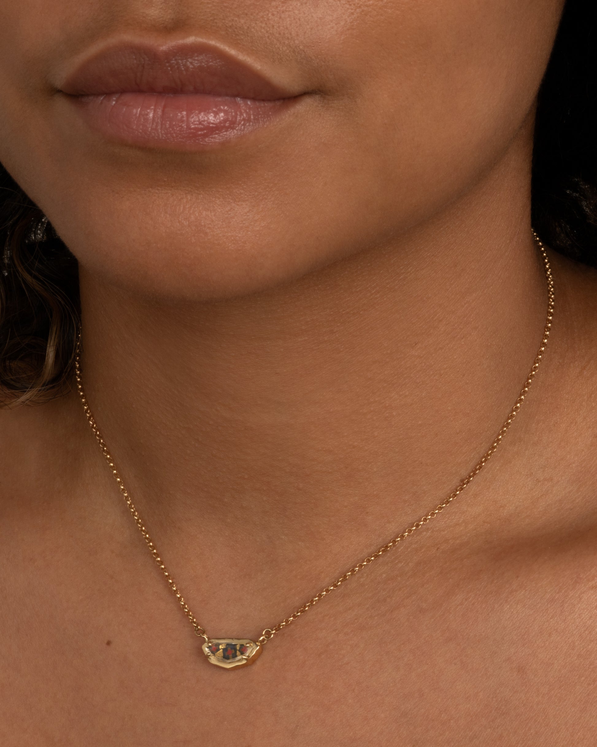 A yellow gold shield shaped necklace with a portrait cut sapphire over micromosaic and goldleaf italian glass and black diamond. Shown worn around the neck.