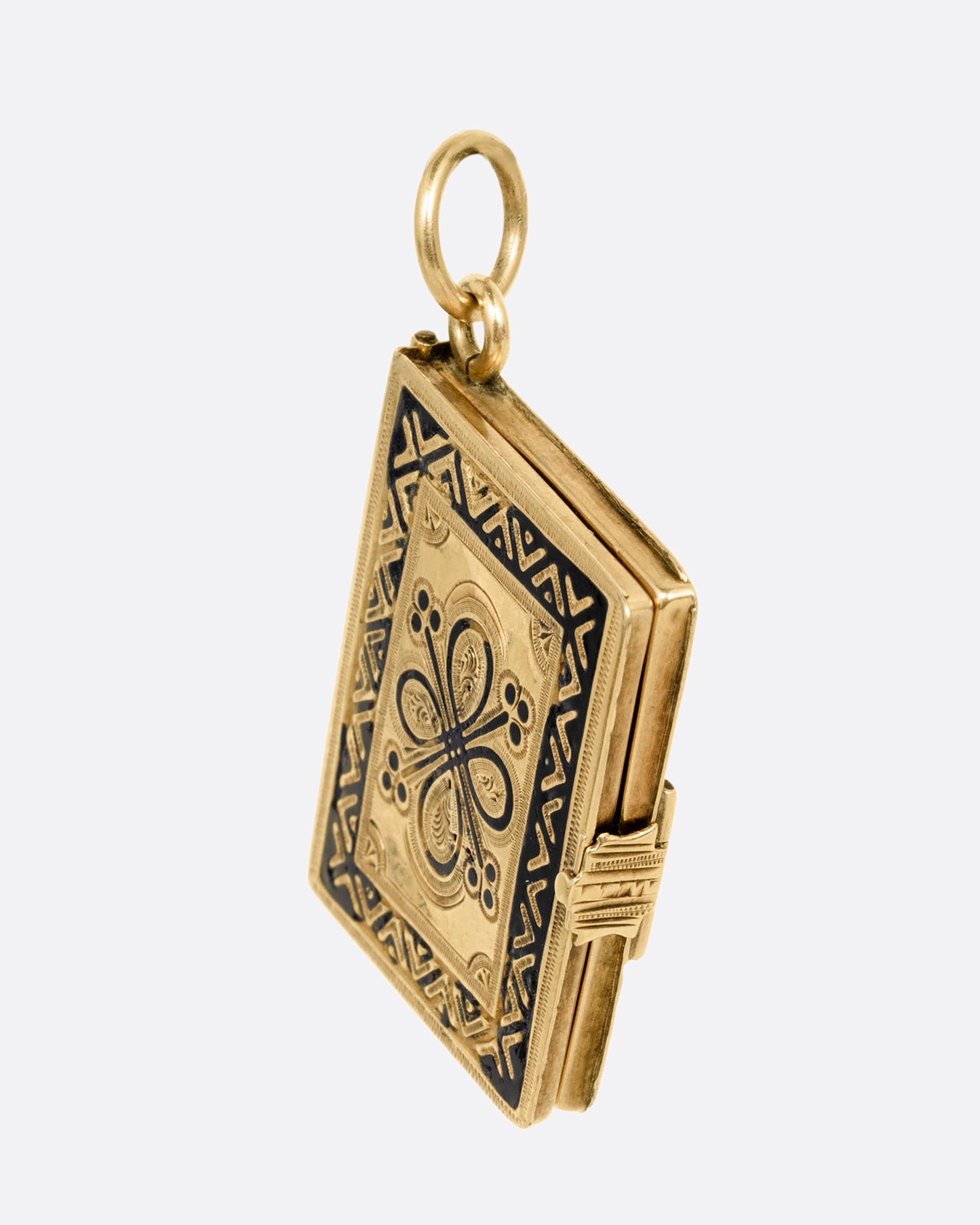 A yellow gold album locket with enamel detailing. It hangs at an angle and has a lock on its binding. Shown from the side. 