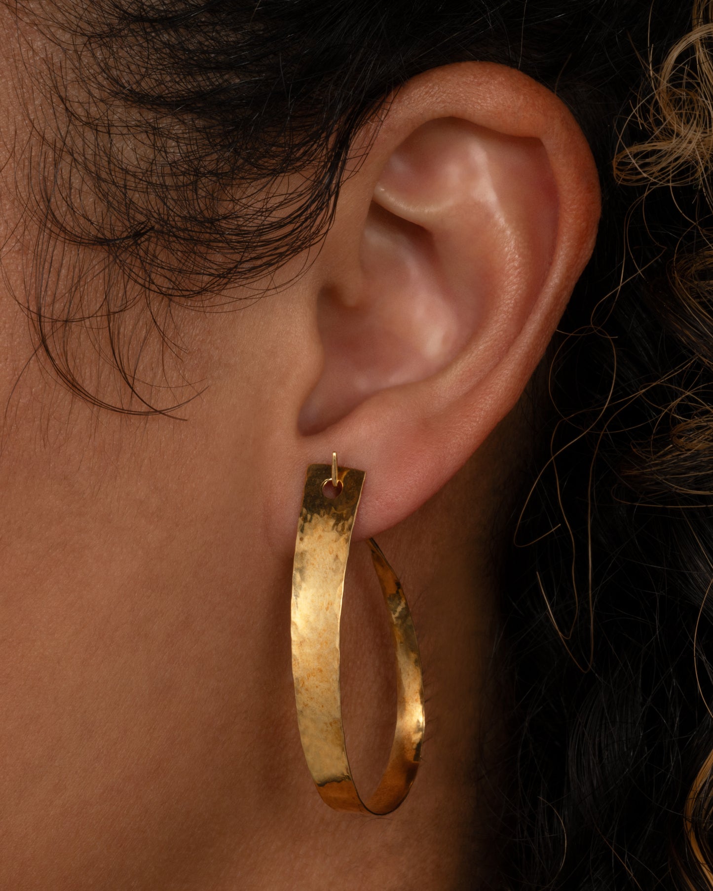 A yellow gold loop earring with a tapered silhouette and minimalist closure, shown on an ear from the front.