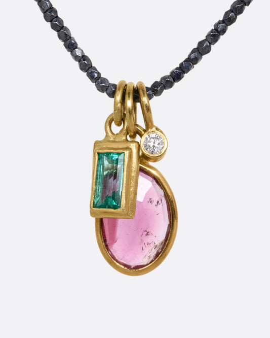 A necklace with three charms; pink tourmaline, emerald, and diamond with oxidized silver beads. Shown from the front.