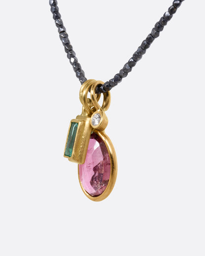 A necklace with three charms; pink tourmaline, emerald, and diamond with oxidized silver beads. Shown from the side.