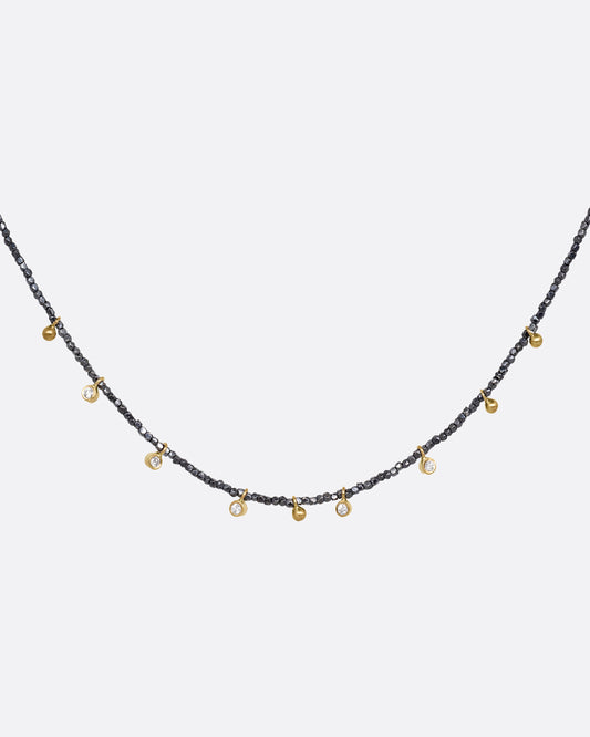 A necklace with five bezel set diamond charms and four gold drops interspersed among oxidized silver beads. Shown from the front.