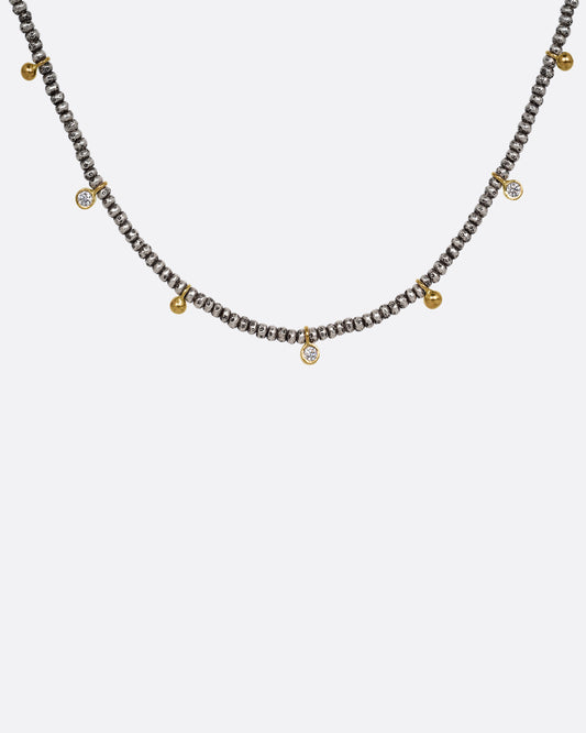 A necklace with nine brilliant cut diamond charms and ten gold drops among oxidized silver beads. Shown from the front.