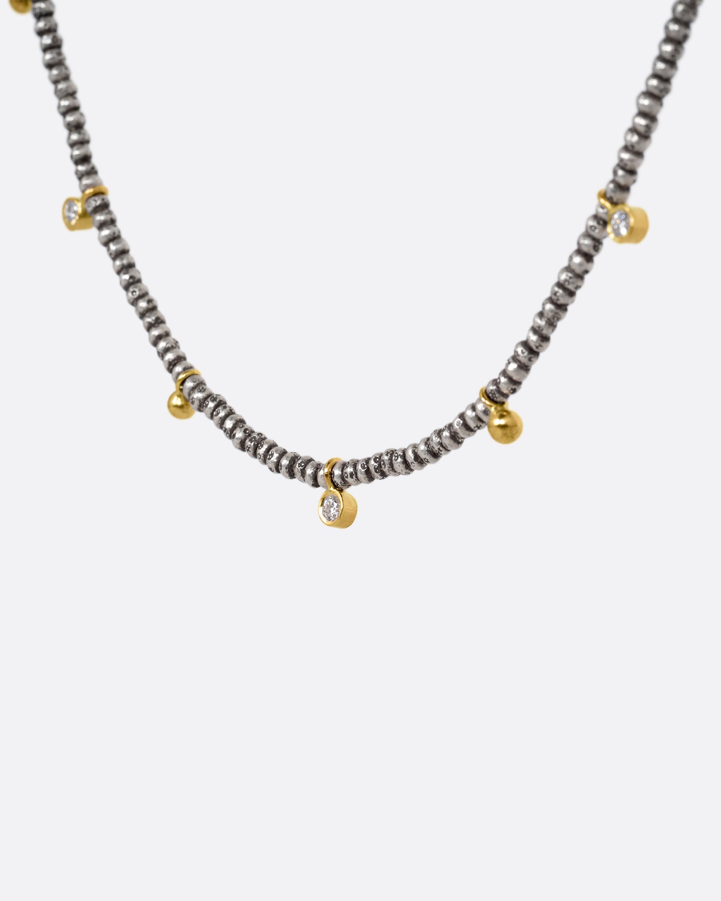 A necklace with nine brilliant cut diamond charms and ten gold drops among oxidized silver beads. Shown from the side.